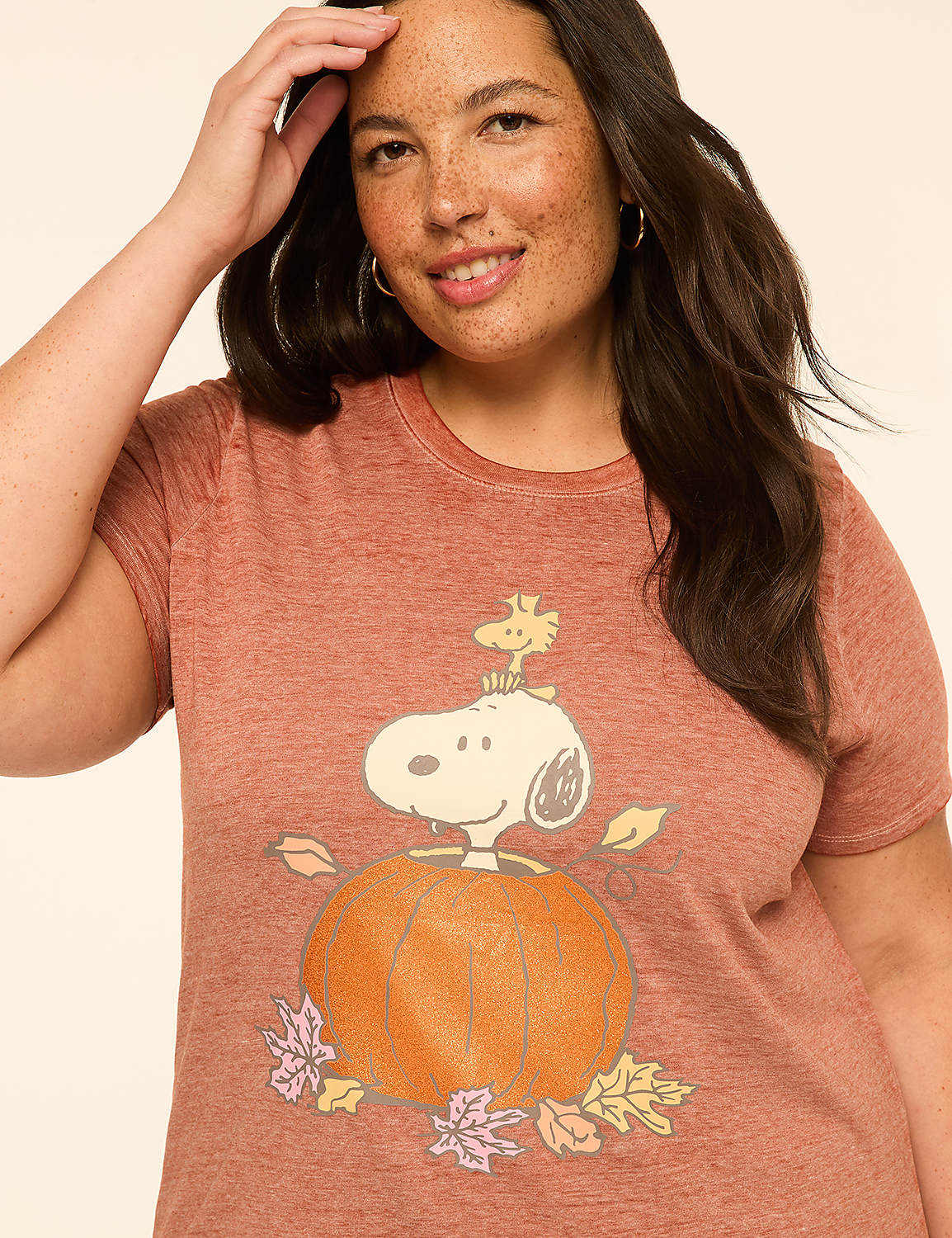 A woman in a rust-colored t-shirt with a Snoopy and Woodstock graphic on a pumpkin smiles against a plain, light background. Product Image 4