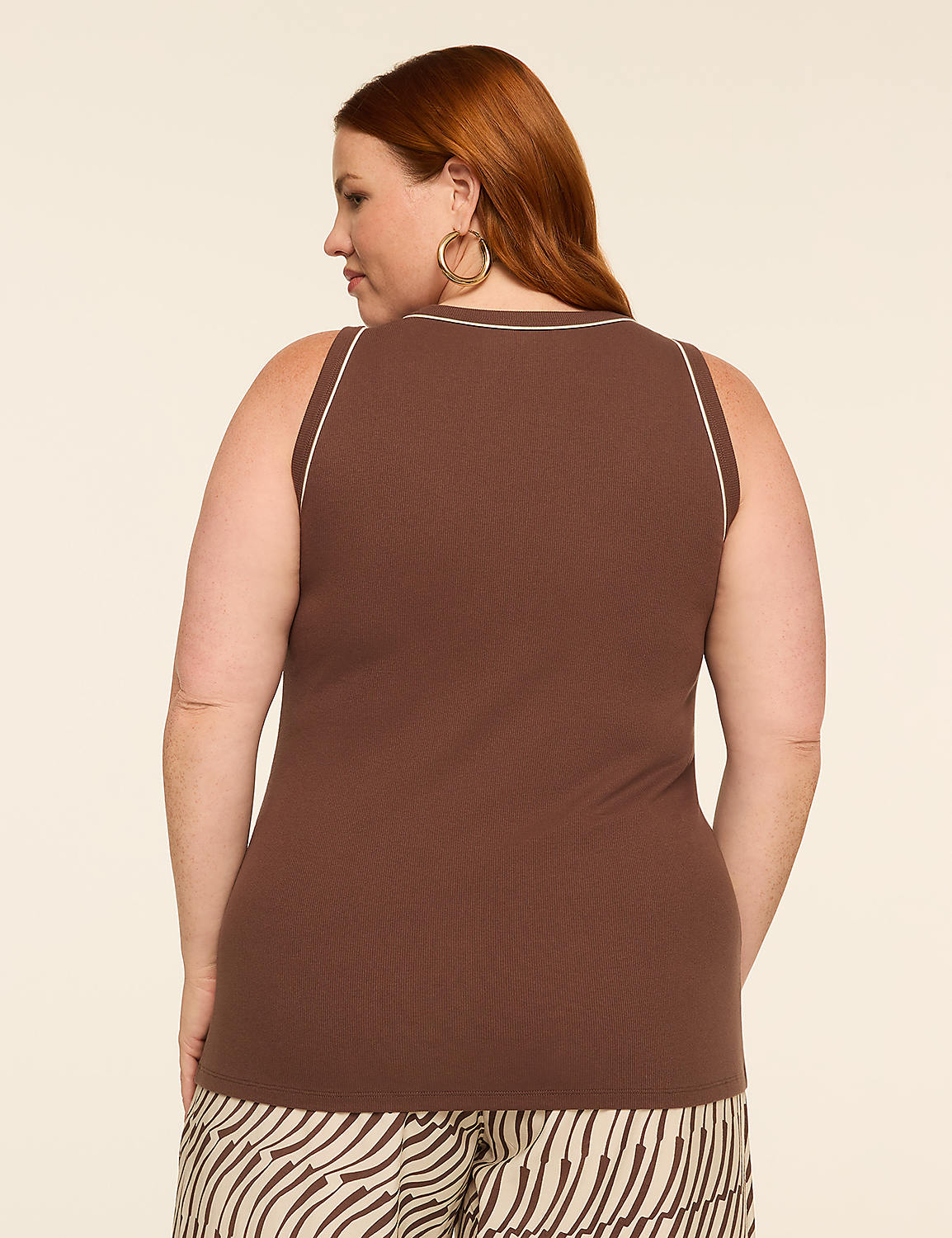 A woman with red hair, wearing a brown ribbed tank top with white trim and patterned pants, stands against a plain beige background. Product Image 2