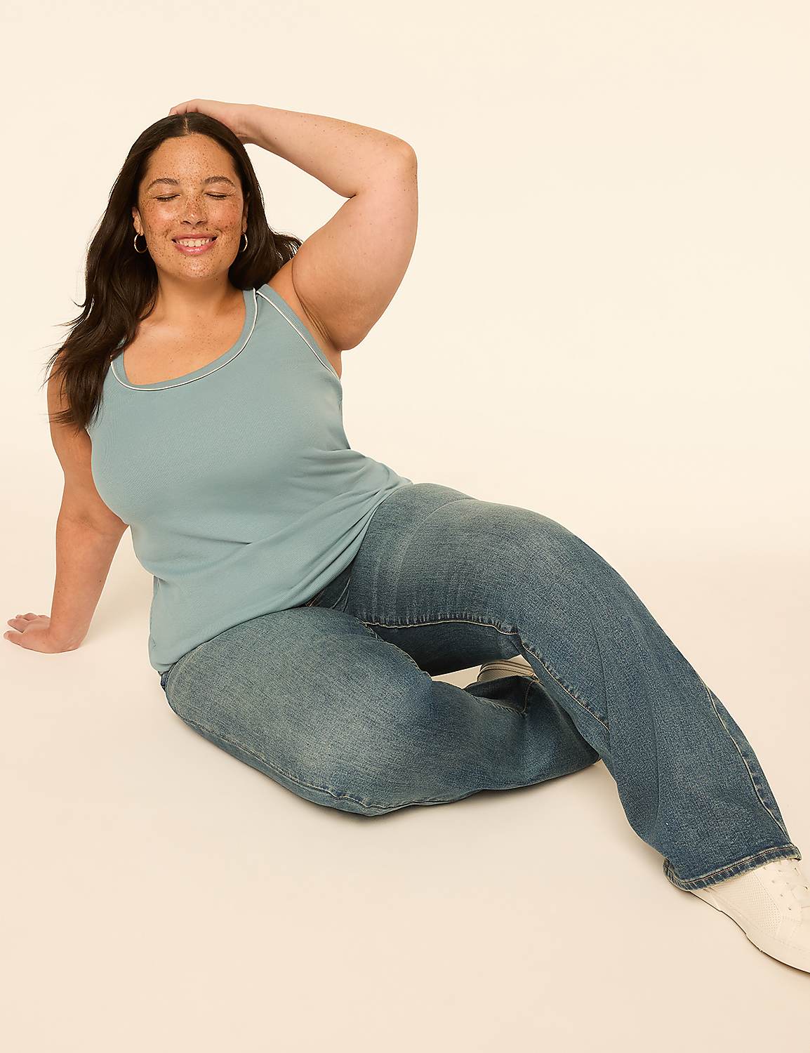 A woman in a blue tank top and jeans sits on a white floor with her arm raised behind her head, against a plain, light background. Product Image 3