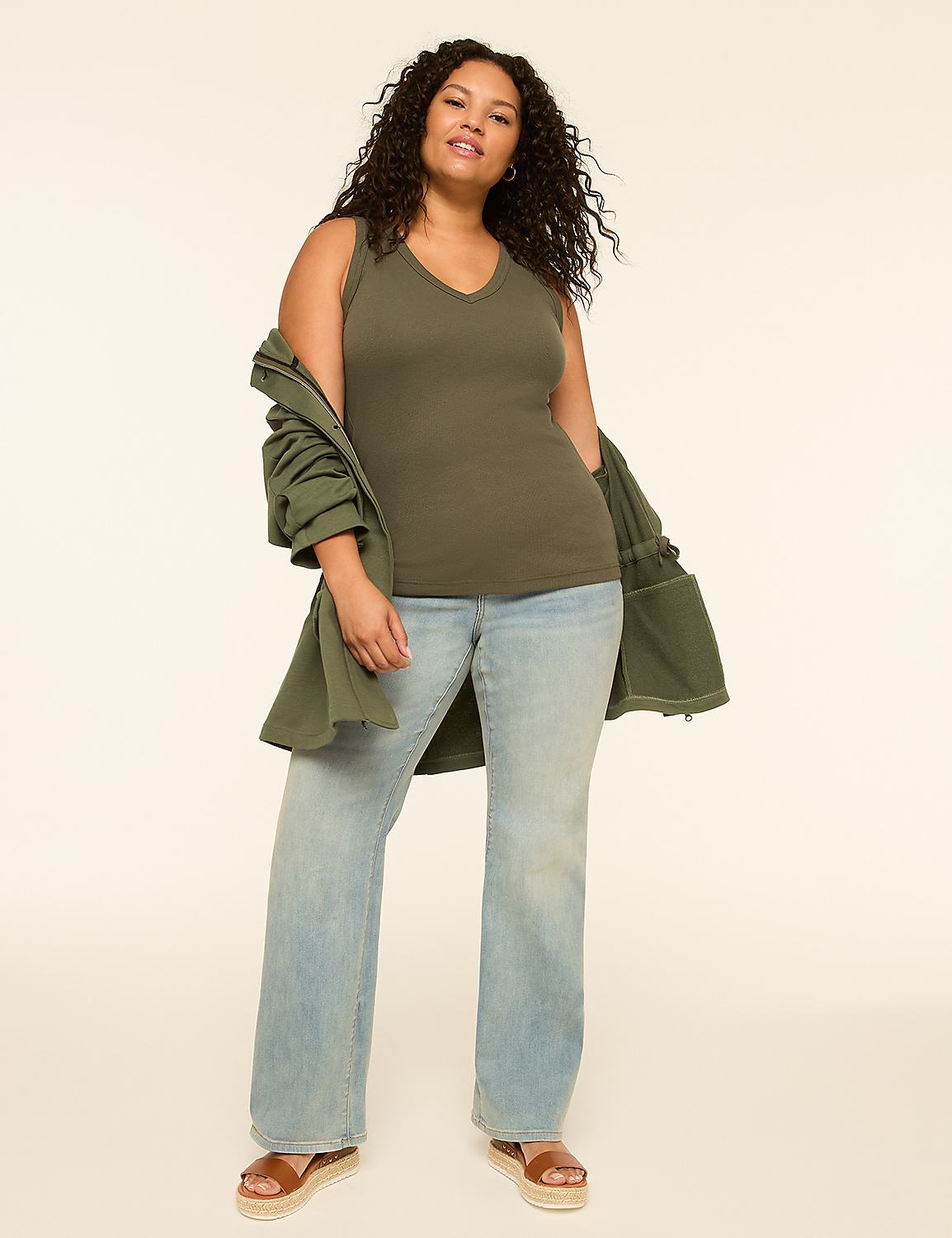 A woman in a green tank top and light wash jeans stands against a plain, light background, with a green jacket draped over her shoulders. Product Image 3
