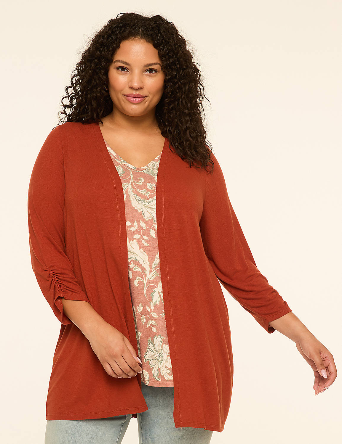 A woman with curly dark hair smiles as she poses in a rust-colored cardigan over a floral print top against a plain cream background. Product Image 1