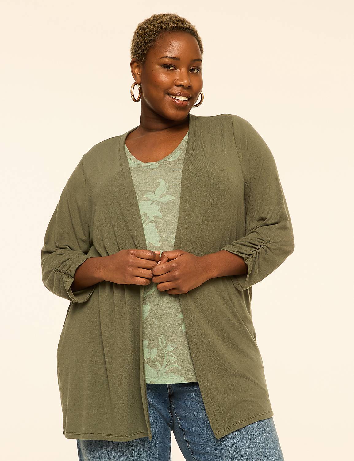 A smiling woman in a green cardigan and floral top stands against a plain, light background. Product Image 1