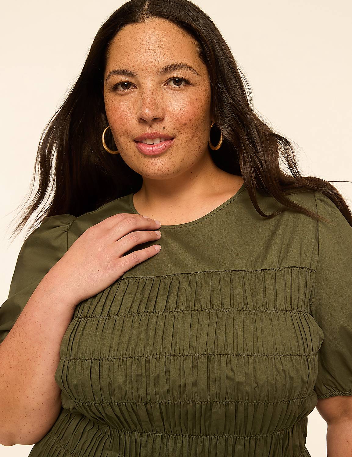 A woman with dark hair and freckles smiles gently in a green top with smocking, against a plain, light background. Product Image 4