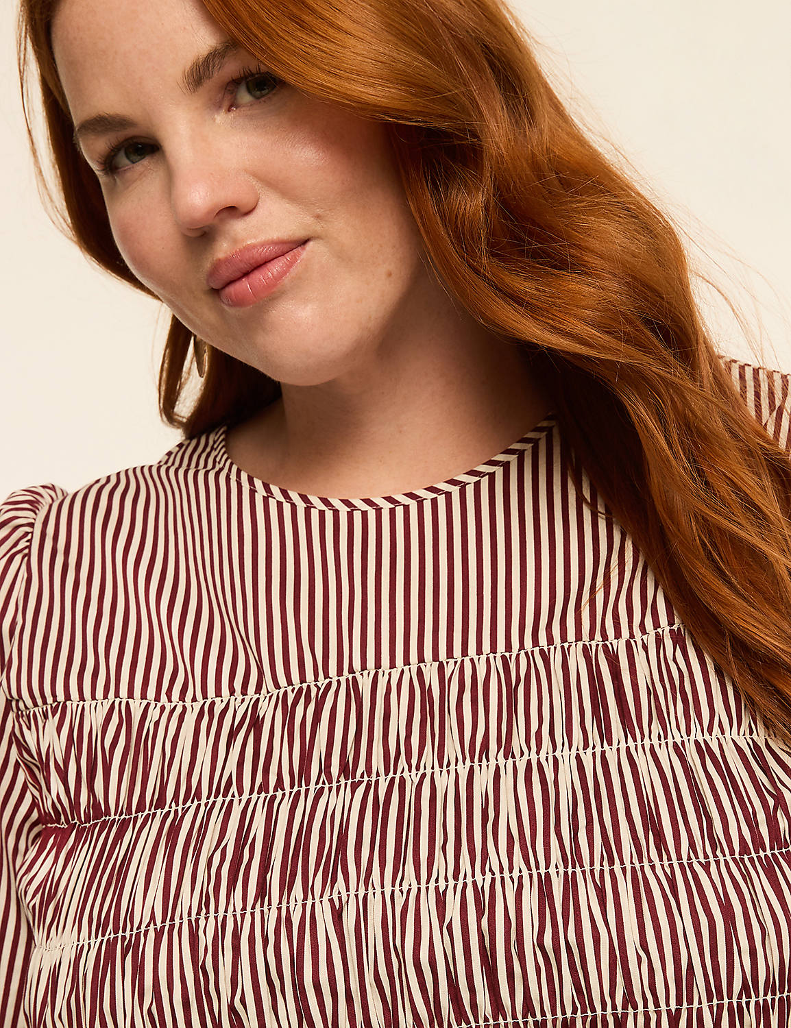 A woman with red hair smiles softly in the foreground, wearing a striped top against a plain, light background. Product Image 4