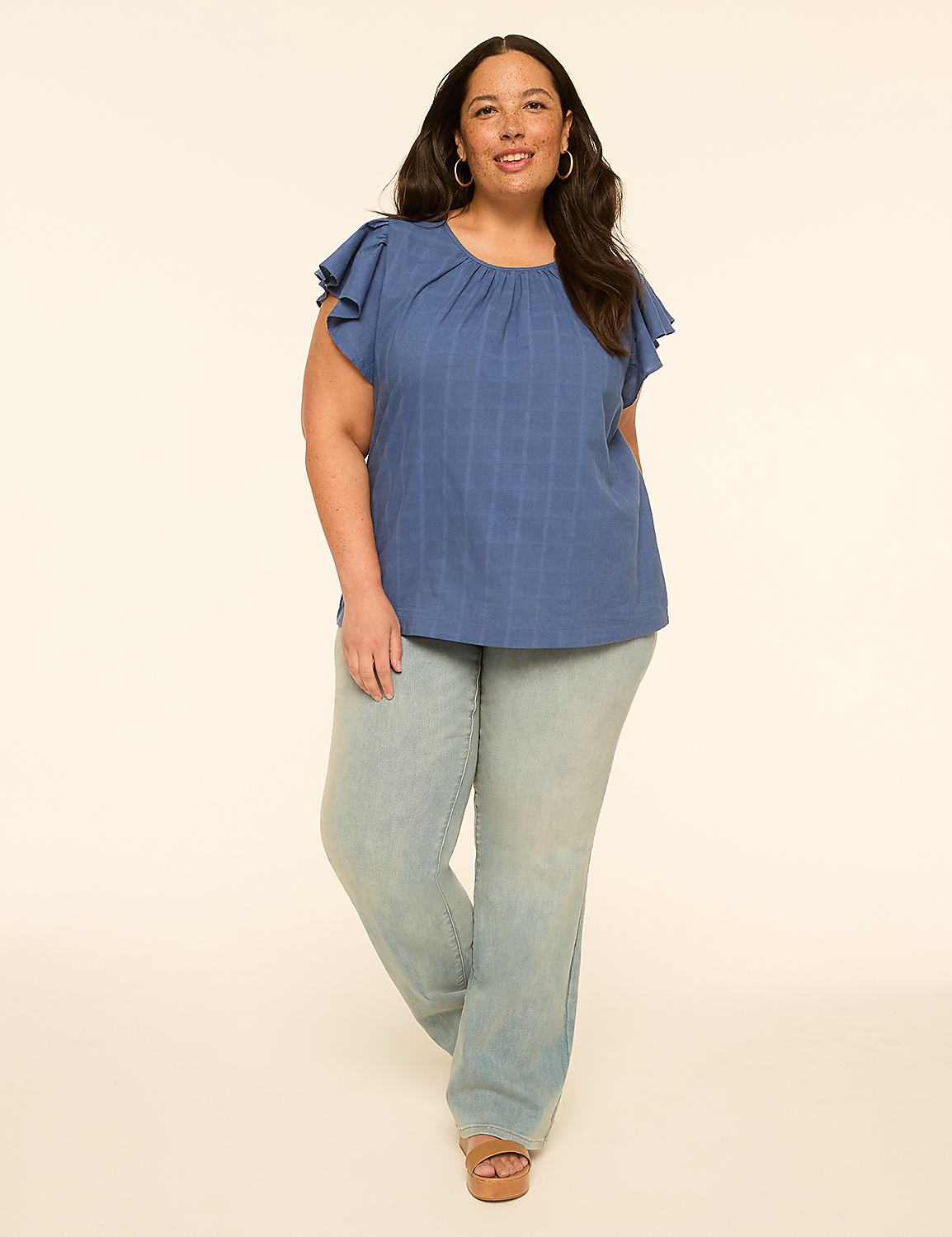 A woman in a blue ruffled-sleeve top and light-wash jeans stands against a plain, light-colored background. Product Image 3