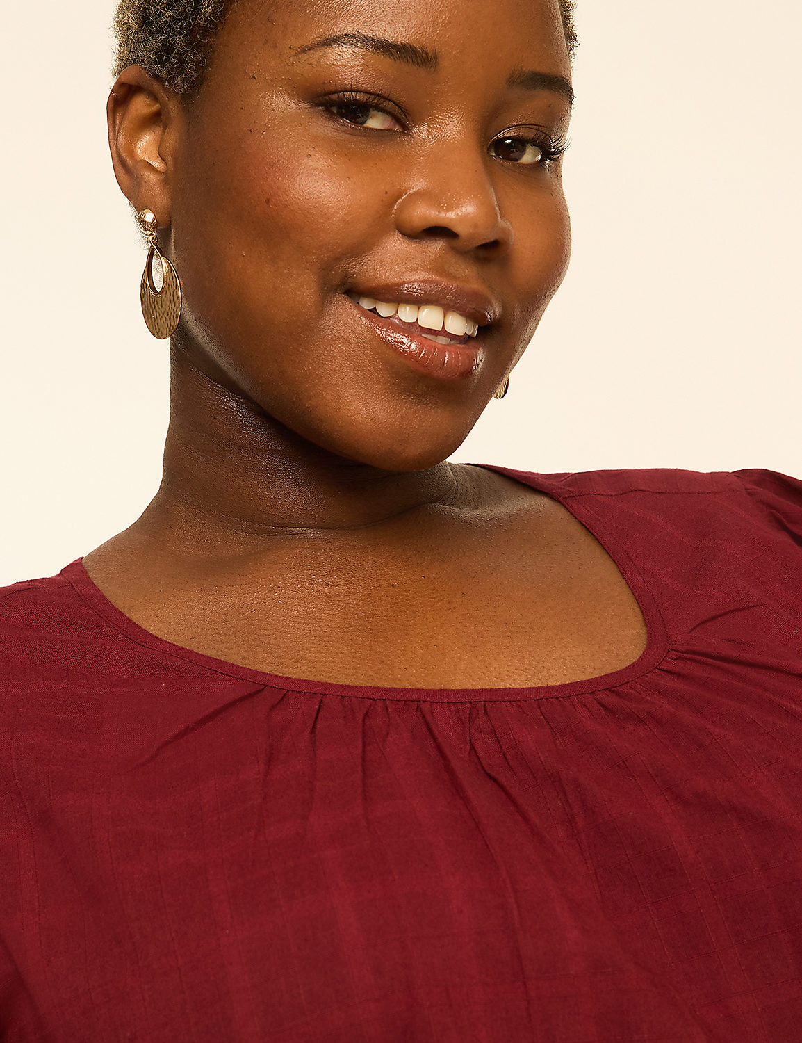 A smiling woman with short, curly hair and large hoop earrings wears a maroon top against a plain, light-colored background. Product Image 4