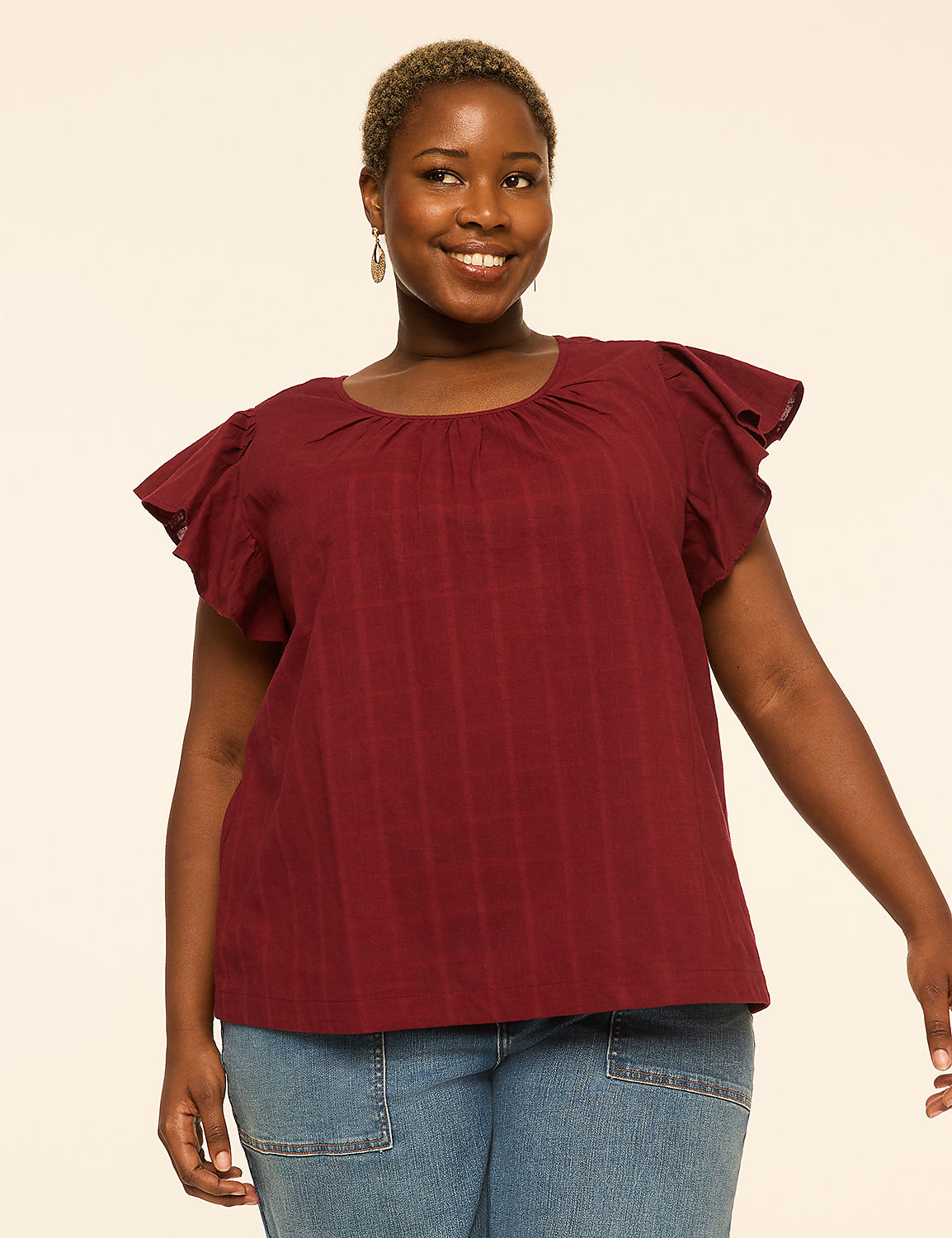 A smiling woman in a maroon ruffled-sleeve top and blue jeans stands against a plain, light-colored background. Product Image 1