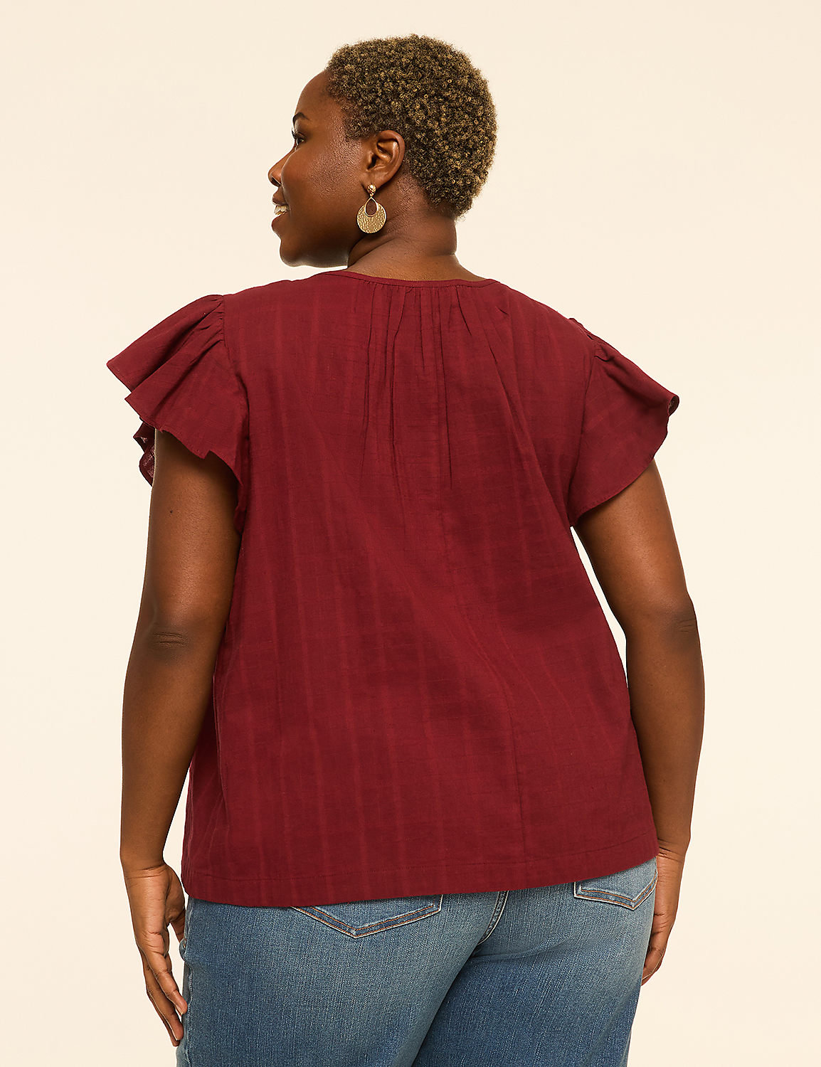 A woman in a maroon flutter-sleeve top and blue jeans stands against a plain, light-colored background. Product Image 2