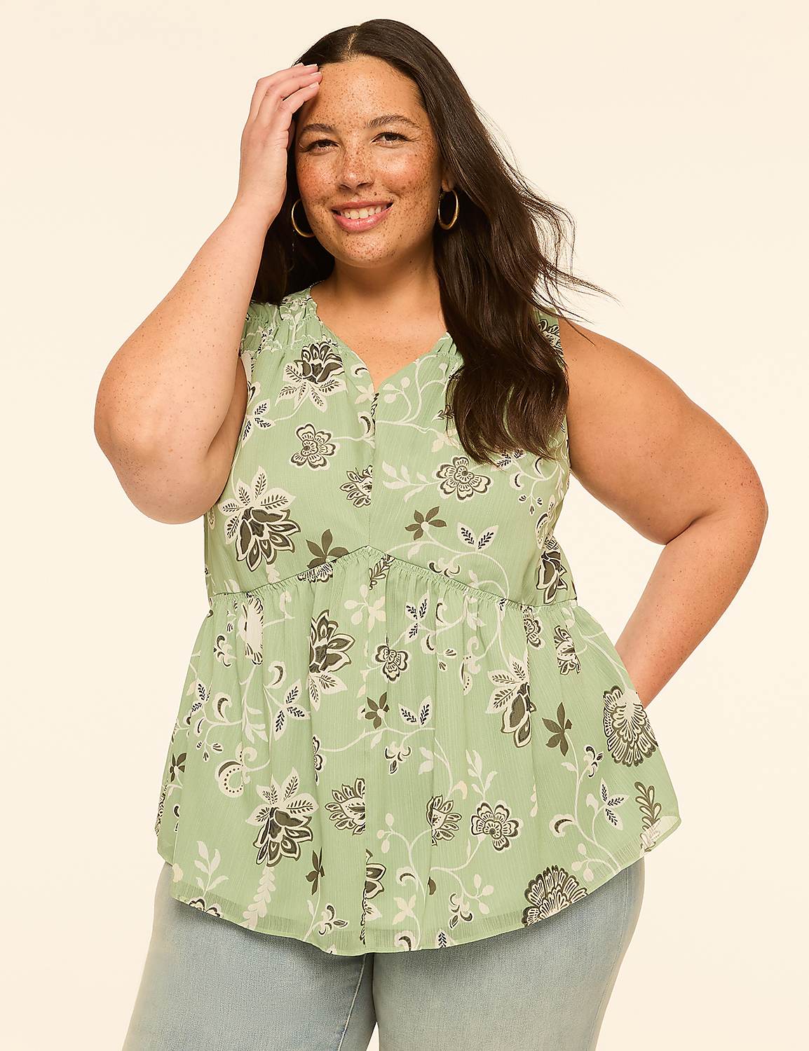 A smiling woman with freckles in a floral peplum top stands against a plain, light-colored background. Product Image 1