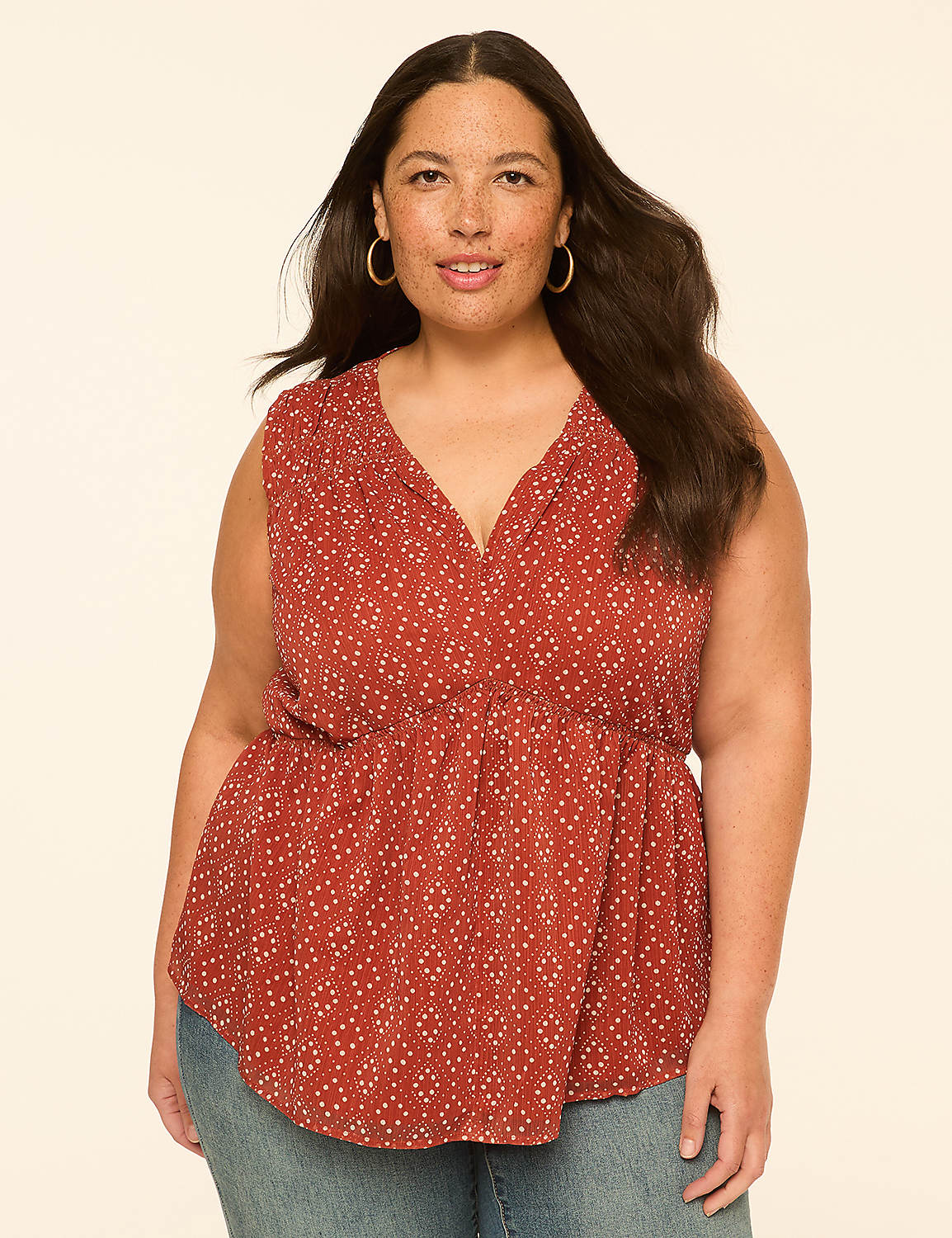 A woman with dark hair and freckles, wearing a rust-colored patterned top and blue jeans, smiles against a plain, light-colored background. Product Image 1