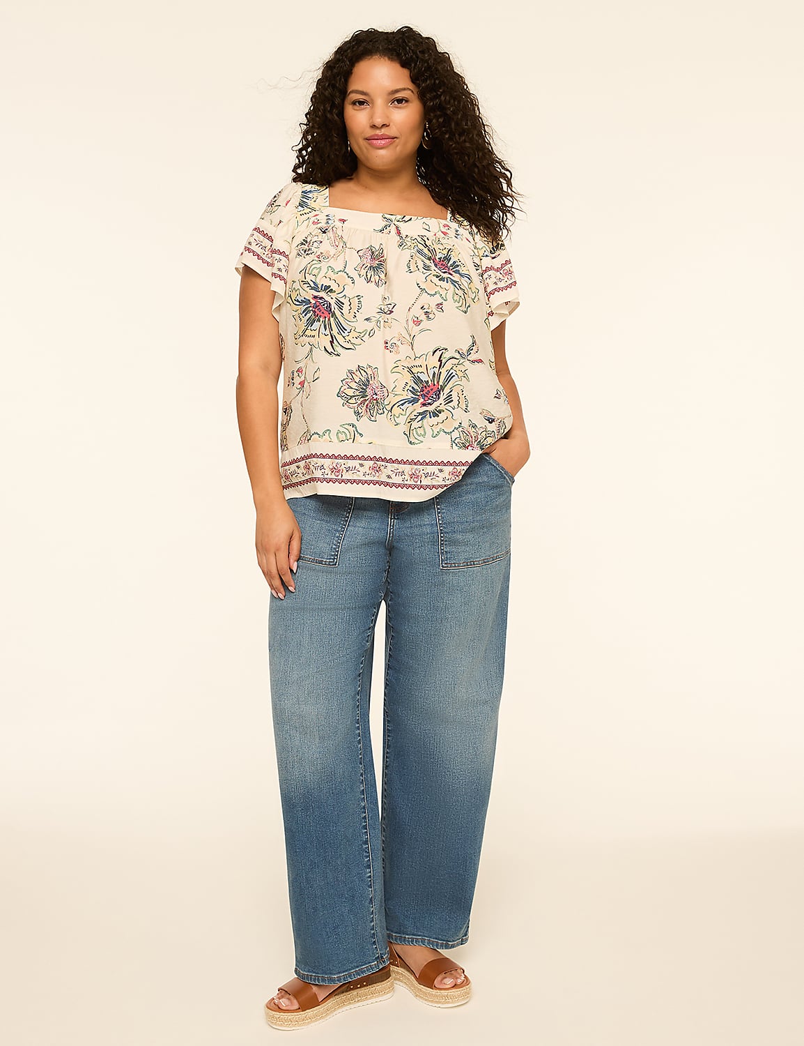 A woman with curly dark hair stands in the foreground wearing a floral print off-the-shoulder top and wide-leg jeans against a plain, light-colored background. Product Image 3
