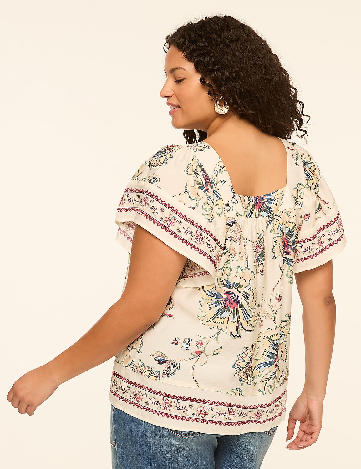A woman in a floral print top and jeans stands against a plain, light-colored background. Product Image 2