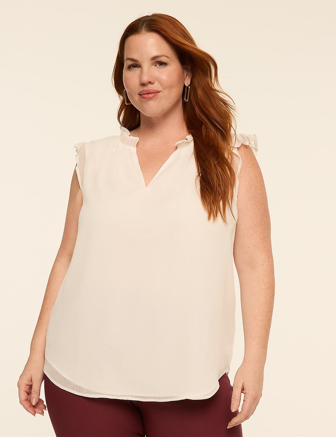 A woman with auburn hair and fair skin, wearing a cream-colored ruffled blouse and maroon pants, poses against a plain beige background. Product Image 1