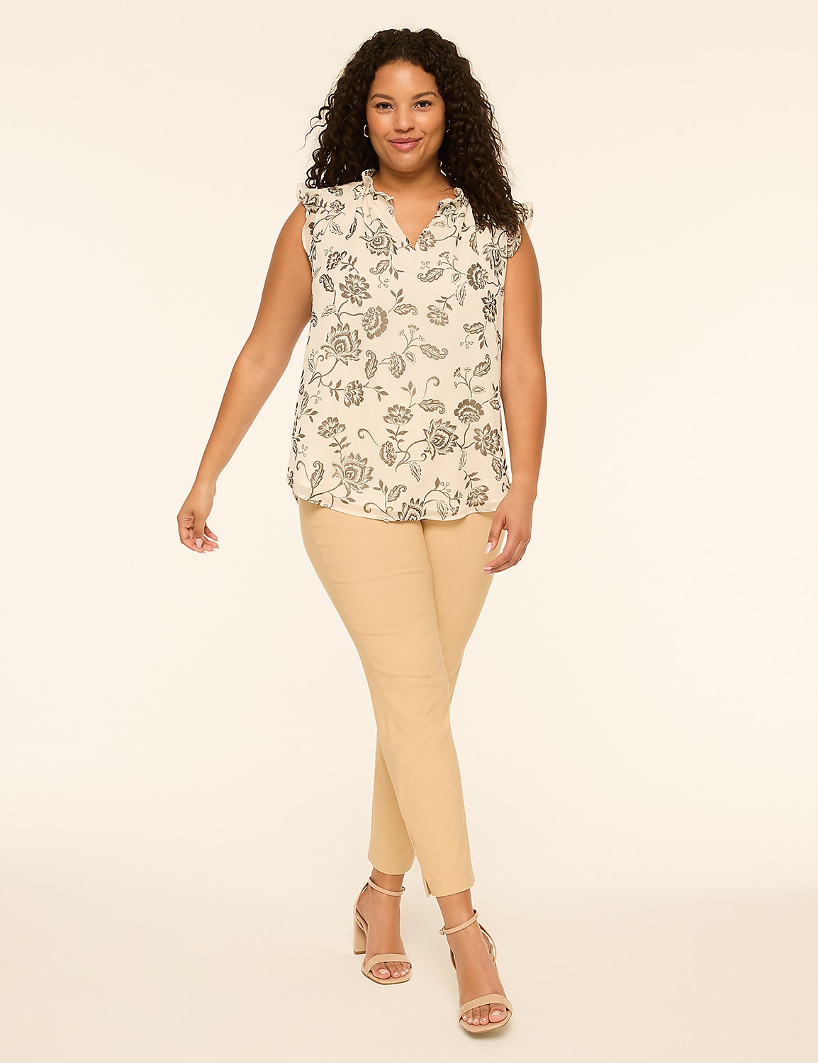 A woman with curly dark hair stands in the foreground wearing a floral print blouse and tan pants, against a plain, light-colored background. Product Image 3