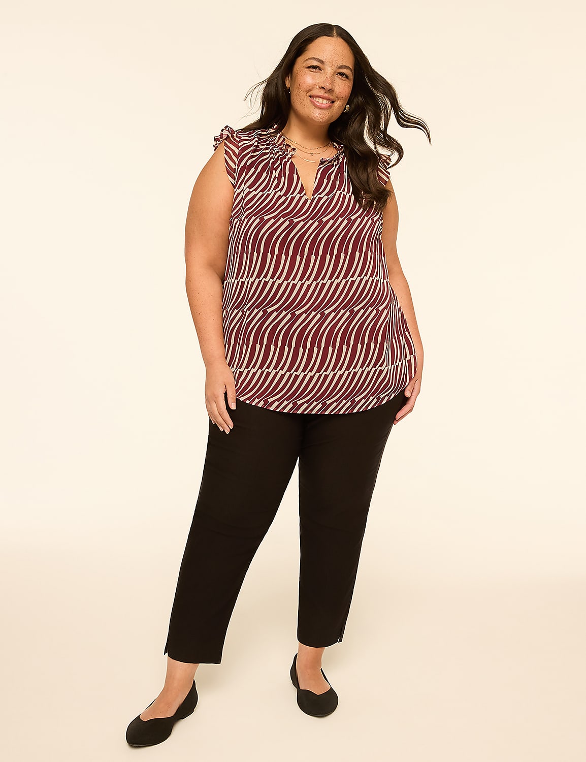 A smiling woman in a patterned top and black pants stands against a plain, light-colored background. Product Image 3