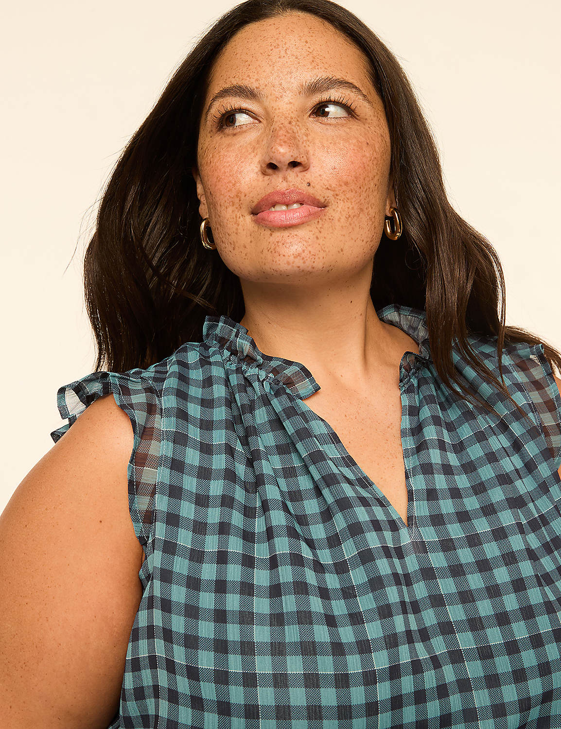 A woman with dark hair and freckles smiles softly, wearing a blue and black checkered top against a plain, light-colored background. Product Image 4