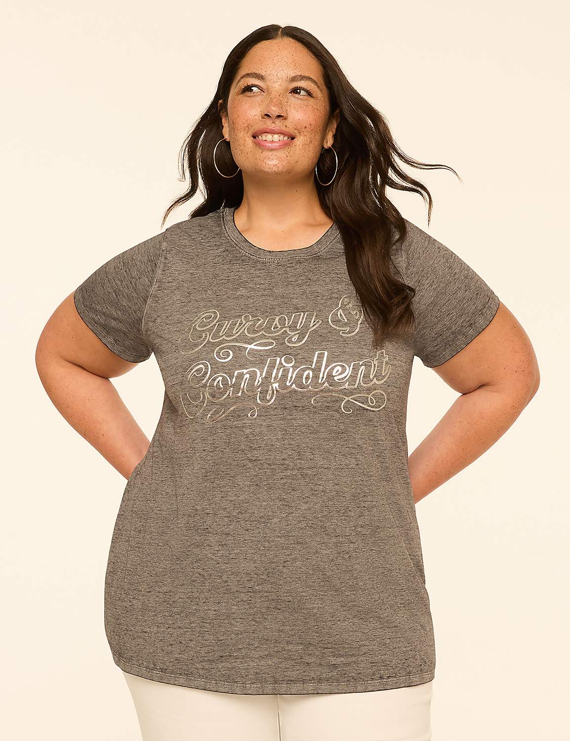 A woman with dark hair and hoop earrings smiles confidently in a grey t-shirt with "Curvy & Confident" written on it, set against a plain, light-colored background. Product Image 1