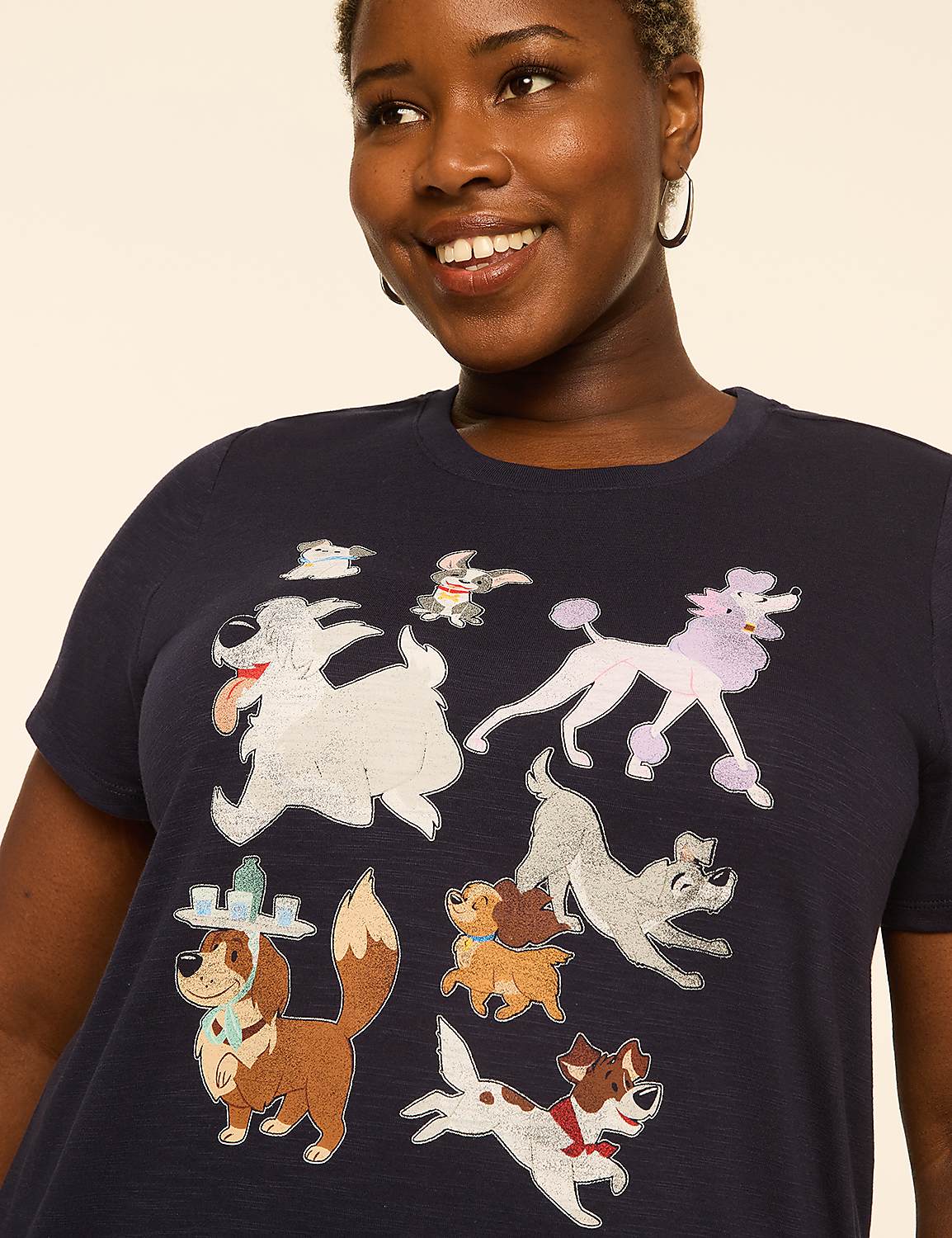 A woman smiles as a variety of cartoon dogs are printed on her dark blue t-shirt against a plain, light background. Product Image 4
