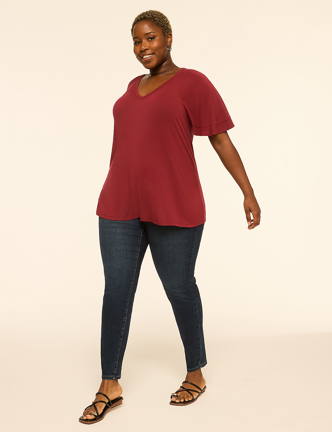 A woman with short, dark hair and a v-neck maroon top stands in dark wash jeans and black sandals against a plain, light-colored background. Product Image 3
