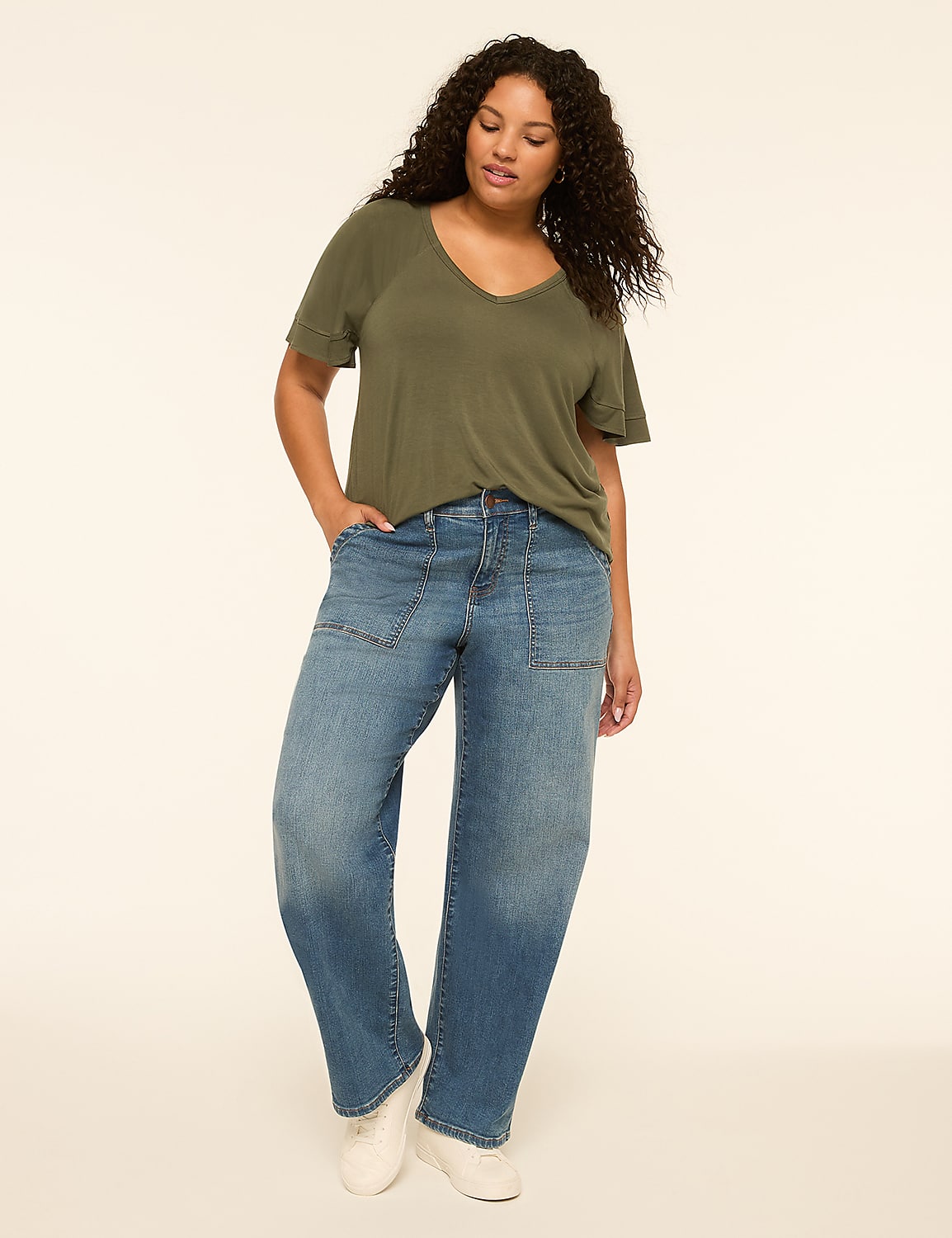 A woman in a green v-neck t-shirt and baggy blue jeans stands against a plain, light-colored background. Product Image 3