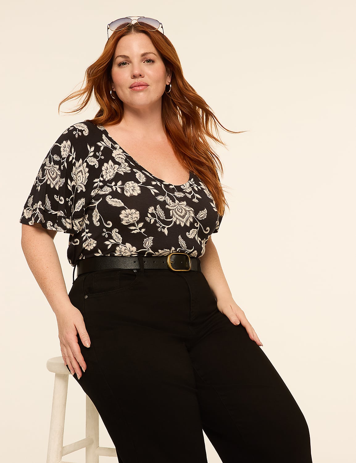 A woman with red hair and a floral top sits on a stool in front of a plain, light-colored background. Product Image 3