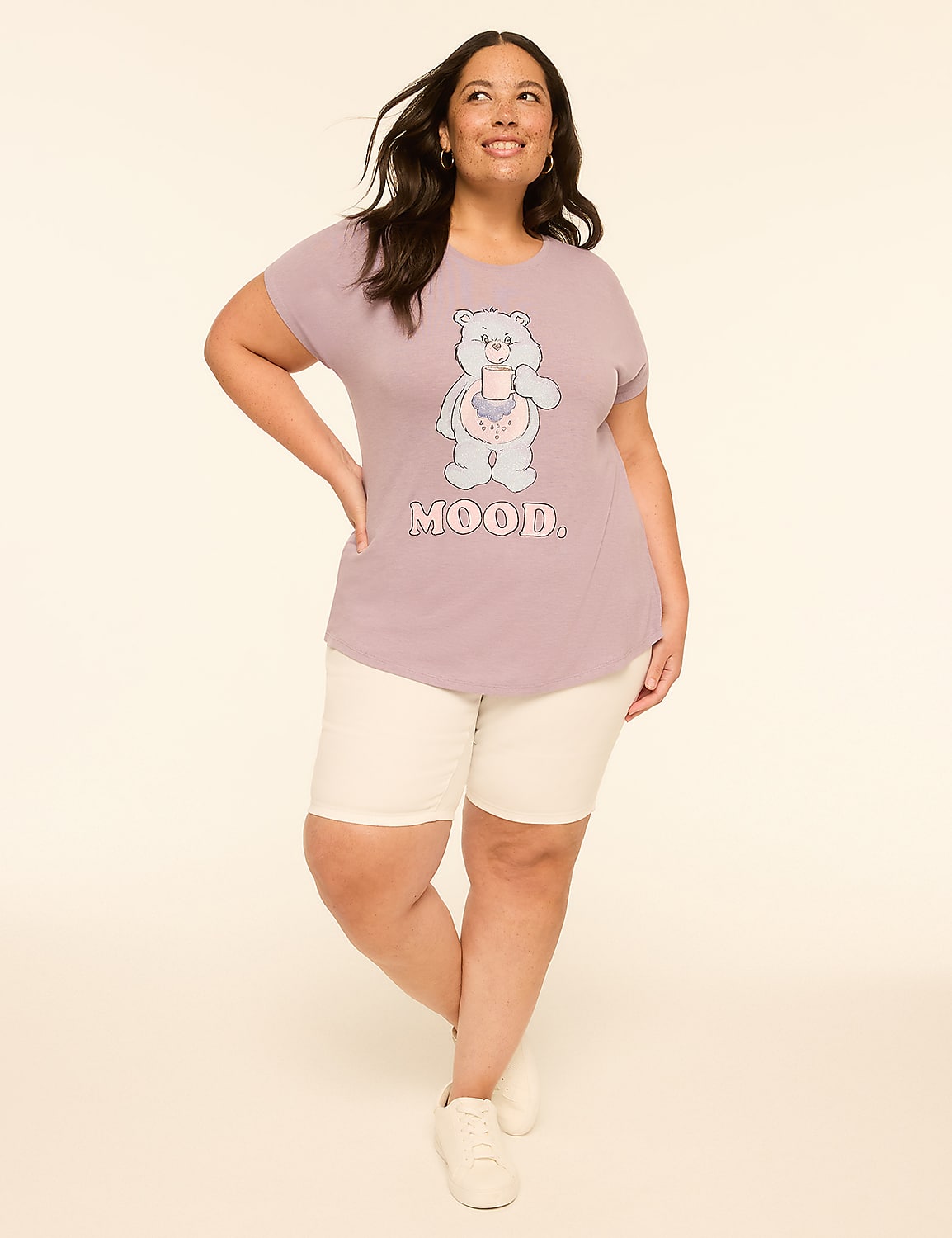 A woman in a purple t-shirt with a Care Bear graphic and white shorts stands against a plain, light-colored background. Product Image 3