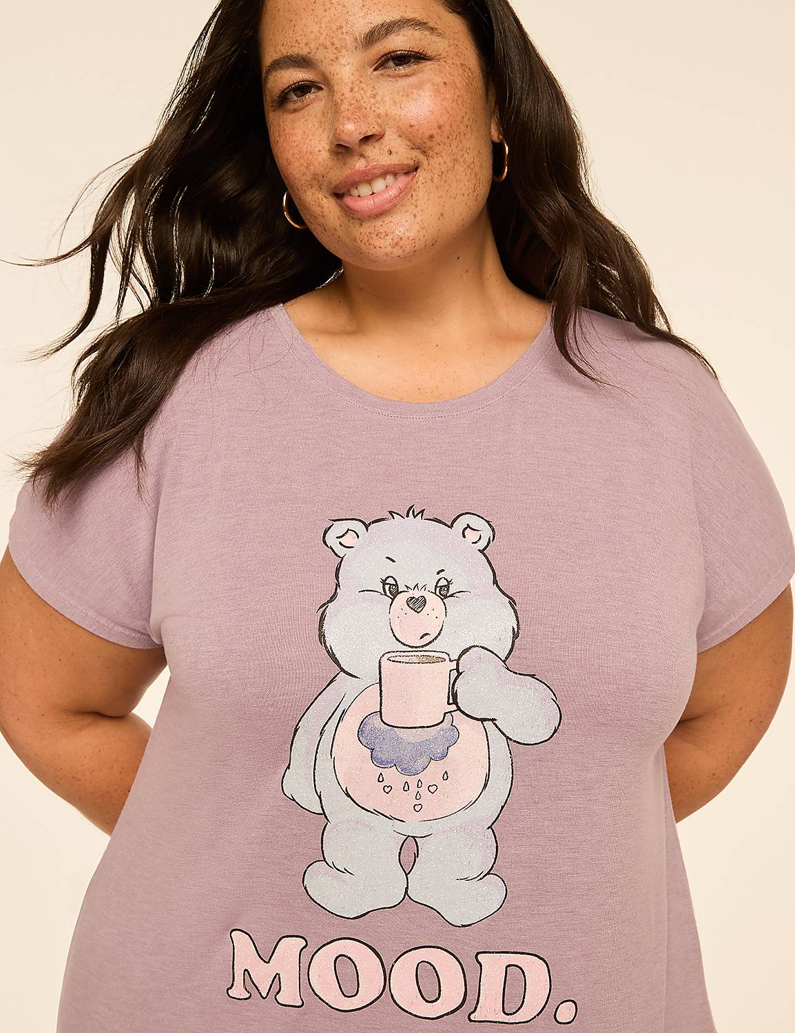 A woman with dark hair and freckles smiles at the camera, wearing a light purple t-shirt with a cartoon bear holding a mug and the word "MOOD." printed below it, against a plain, light-colored background. Product Image 4