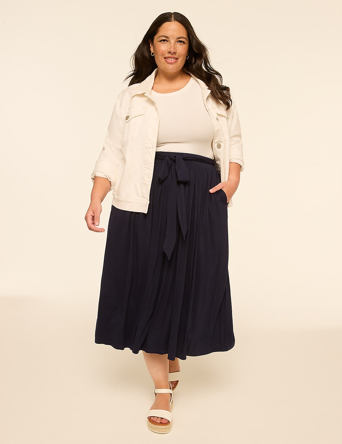 A woman in a white jacket and navy skirt walks forward against a plain, light-colored background. Product Image 3