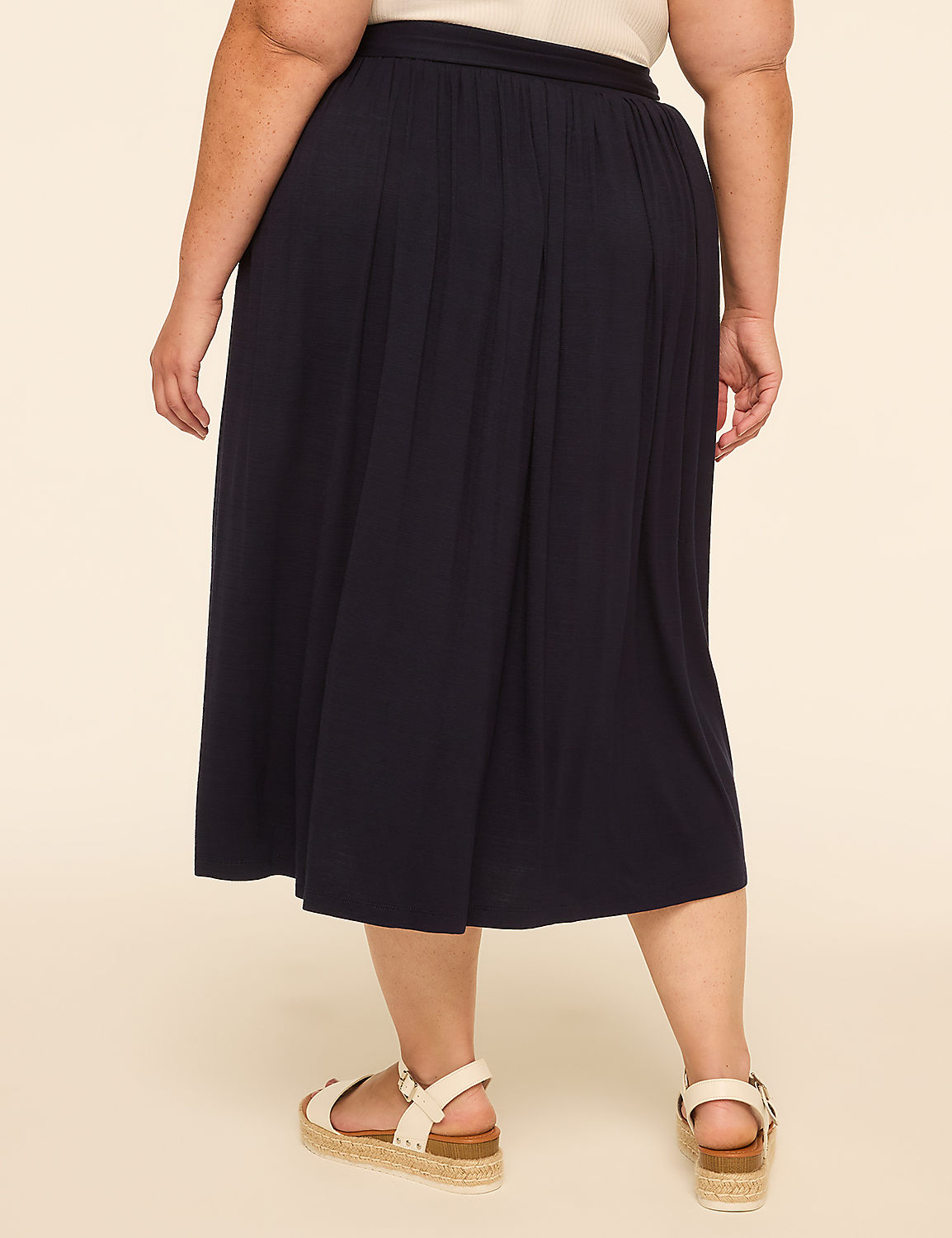 A person wearing a dark blue pleated skirt and white sandals stands against a plain beige background. Product Image 2