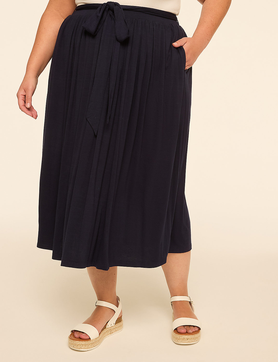 A woman in a navy blue skirt and white sandals stands against a plain beige background. Product Image 1