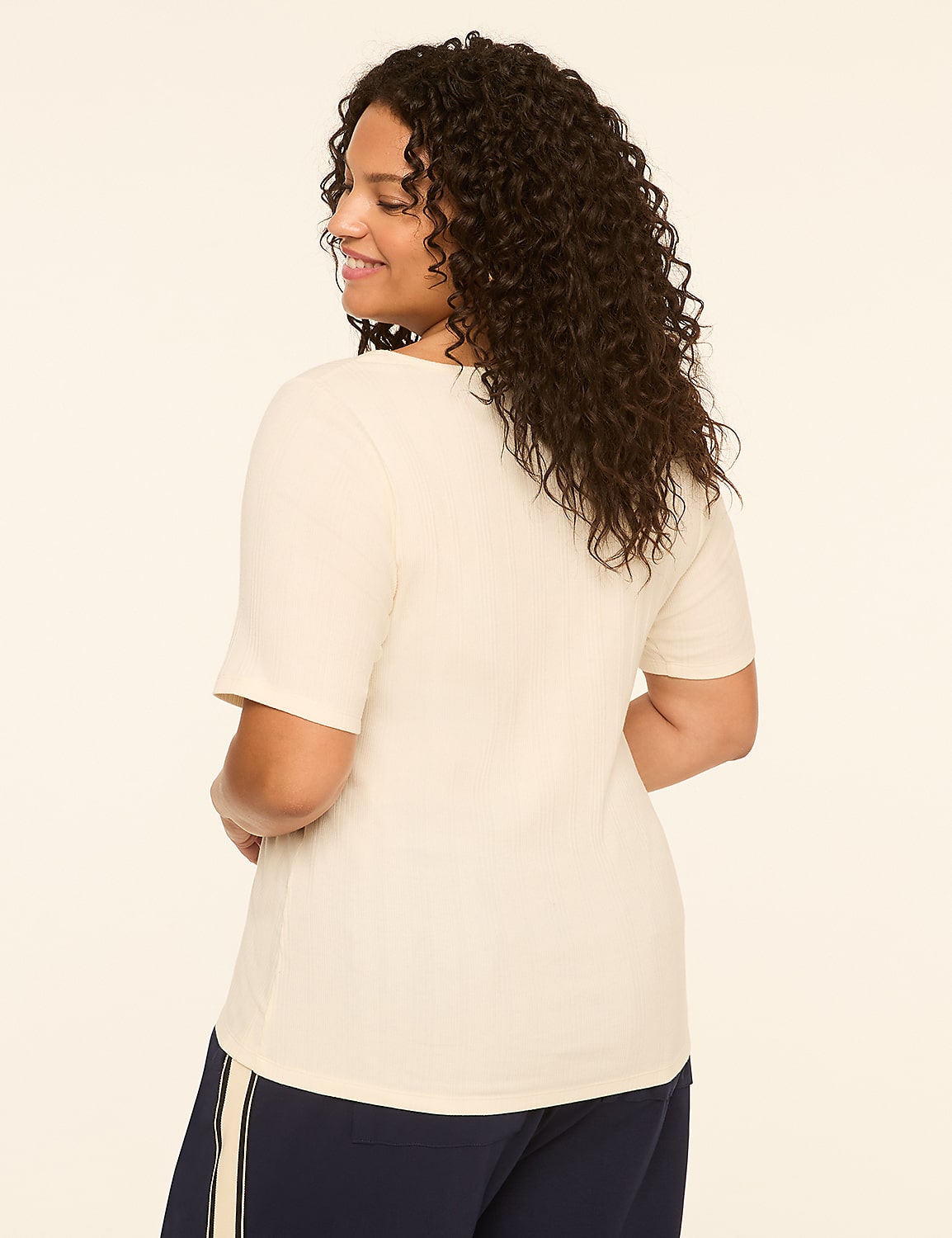 A woman in a cream-colored t-shirt and navy pants stands against a plain, light-colored background. Product Image 2