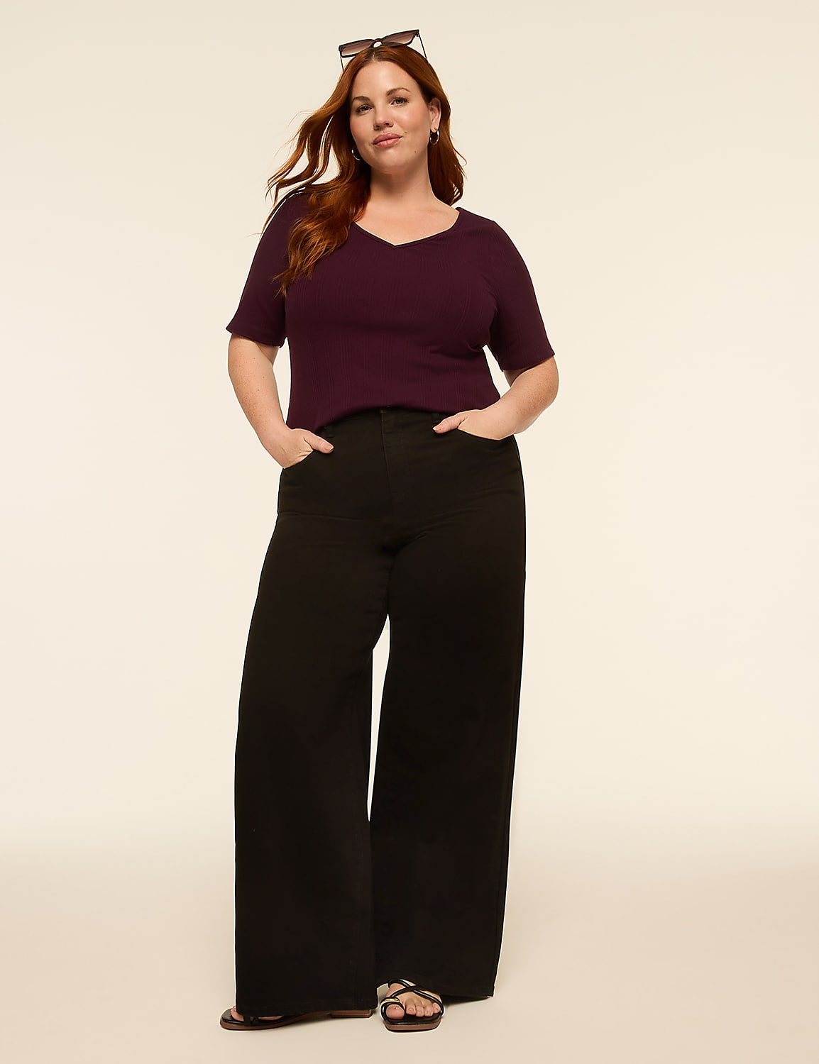 A woman with auburn hair and sunglasses perched on her head stands with her hands in the pockets of her wide-leg black pants and a plum v-neck shirt against a plain, light-colored background. Product Image 3