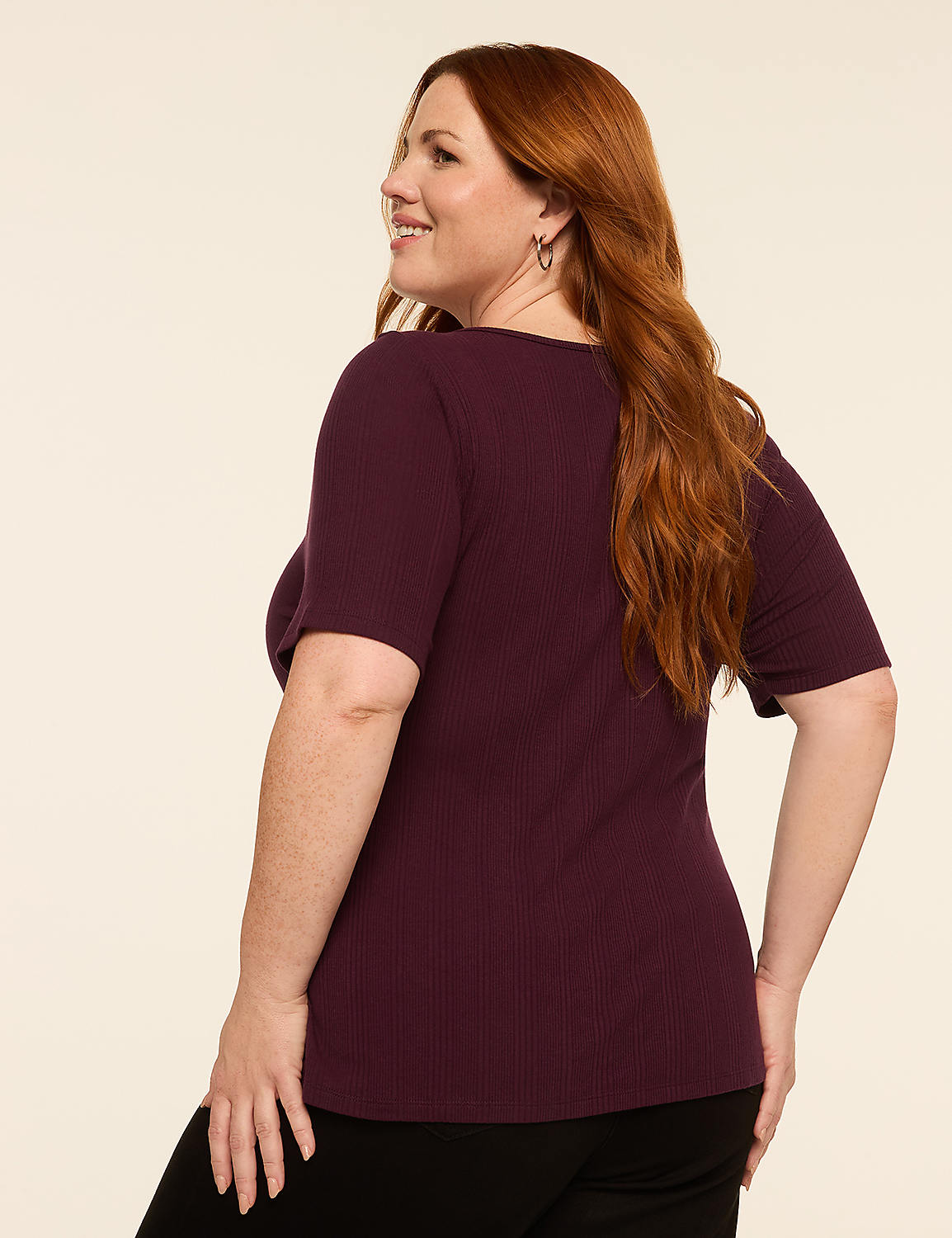 A woman with long, wavy red hair, wearing a burgundy ribbed t-shirt and black pants, smiles as she poses against a plain, light-colored background. Product Image 2