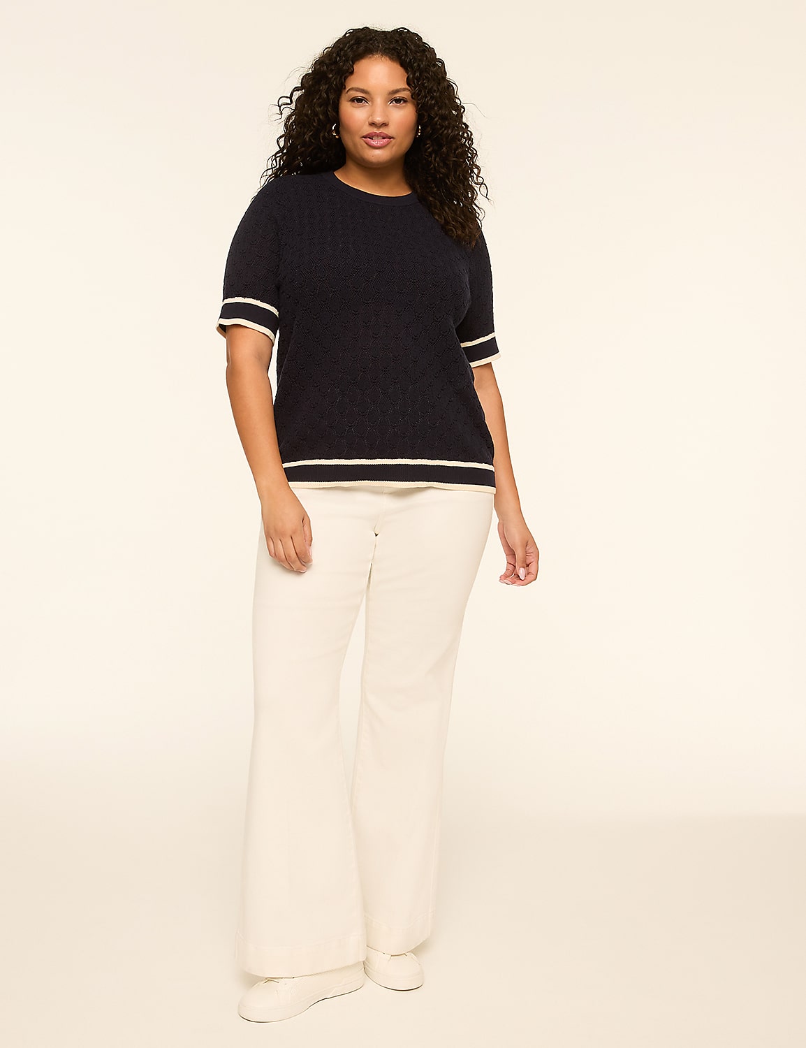 A woman in a navy sweater and white pants stands against a plain, light-colored background. Product Image 3