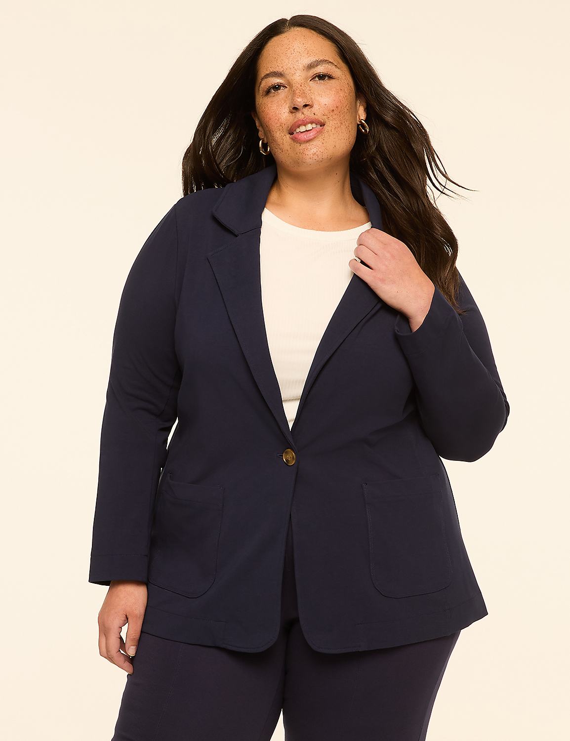 A woman in a navy blazer stands against a plain, light-colored background. Product Image 1