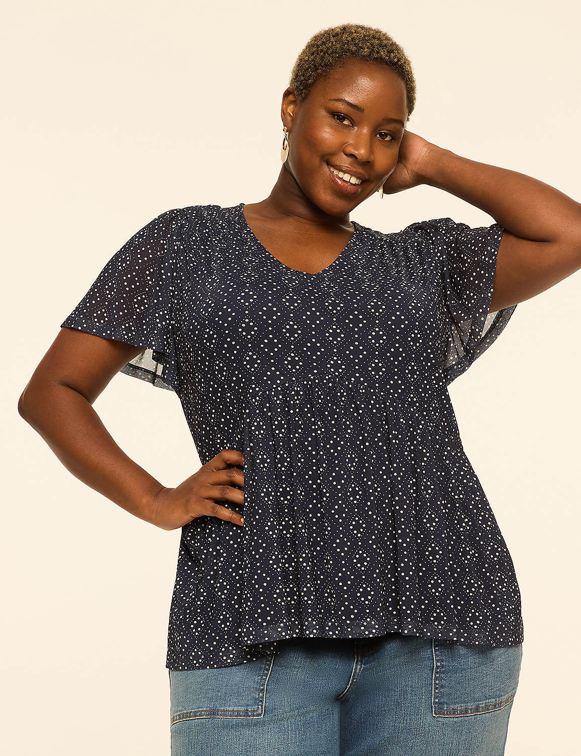 A smiling woman with short, blonde hair and a patterned blue top poses with her hand on her hip against a plain, light-colored background. Product Image 1