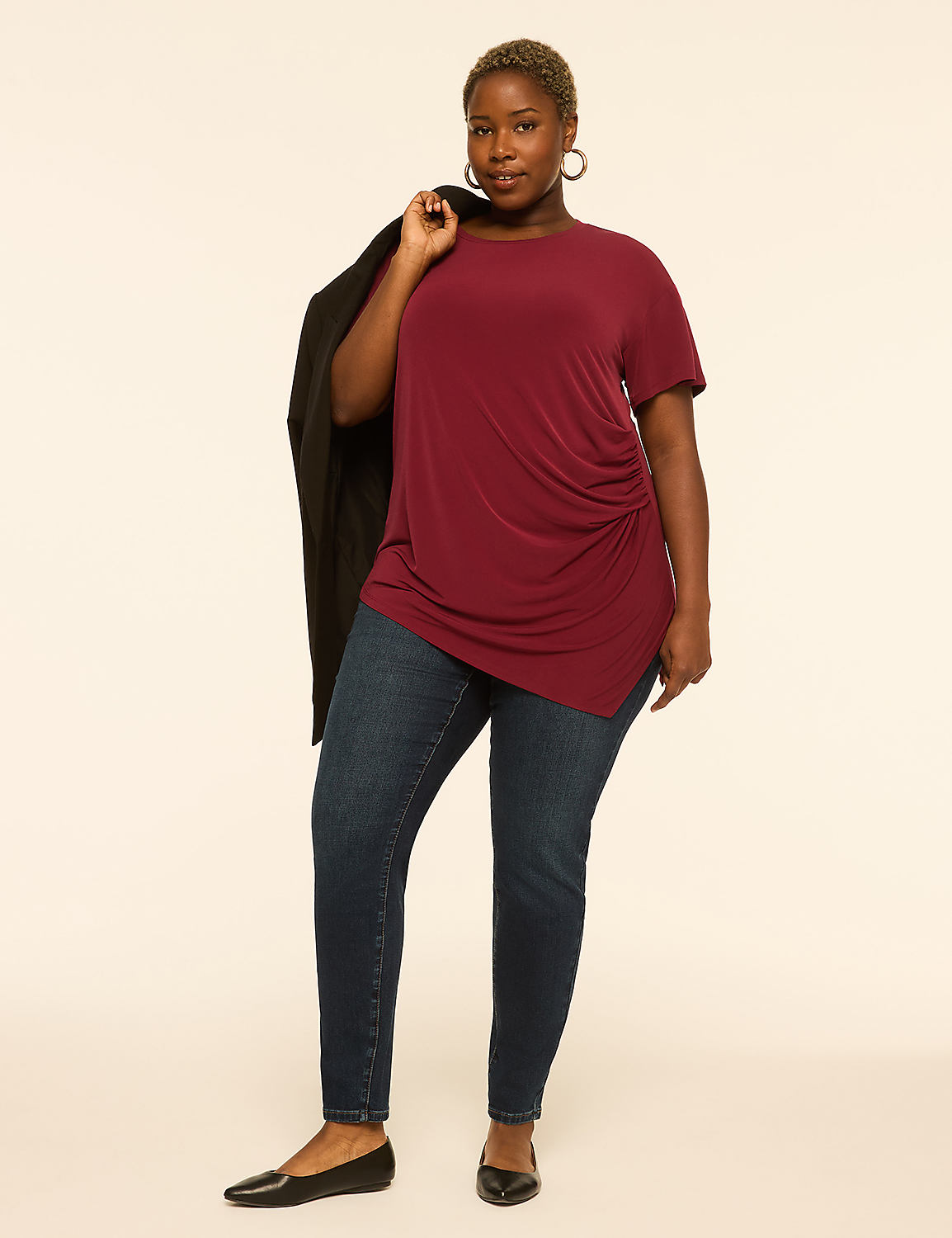 A woman in a maroon top and dark jeans stands against a plain, light background, with a black blazer draped over her shoulder. Product Image 3