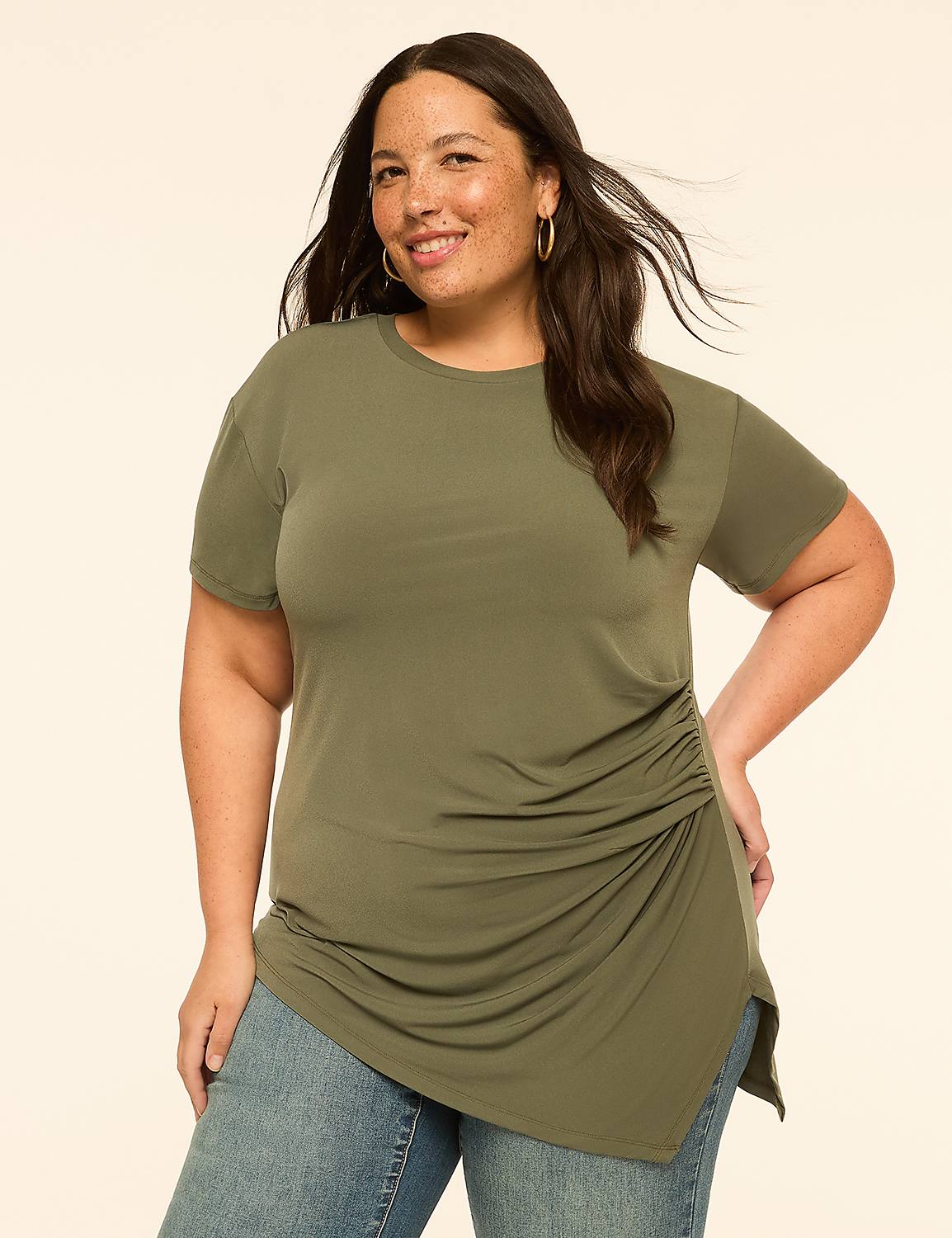 A smiling woman in a ruched olive green top and jeans stands against a plain, light-colored background. Product Image 1