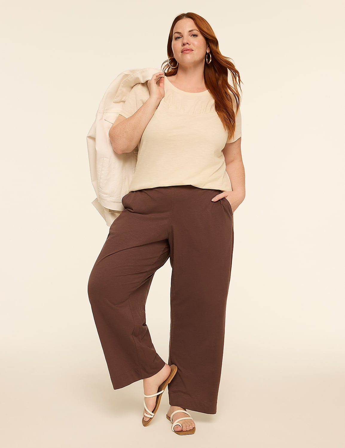 A woman in a cream top and brown pants poses with a jacket draped over her shoulder against a plain, light background. Product Image 3