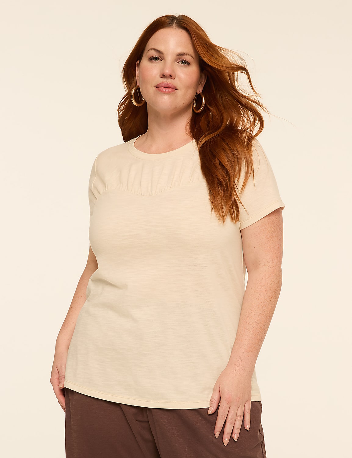 A woman with red hair and hoop earrings stands in the foreground against a plain, light-colored background. Product Image 1