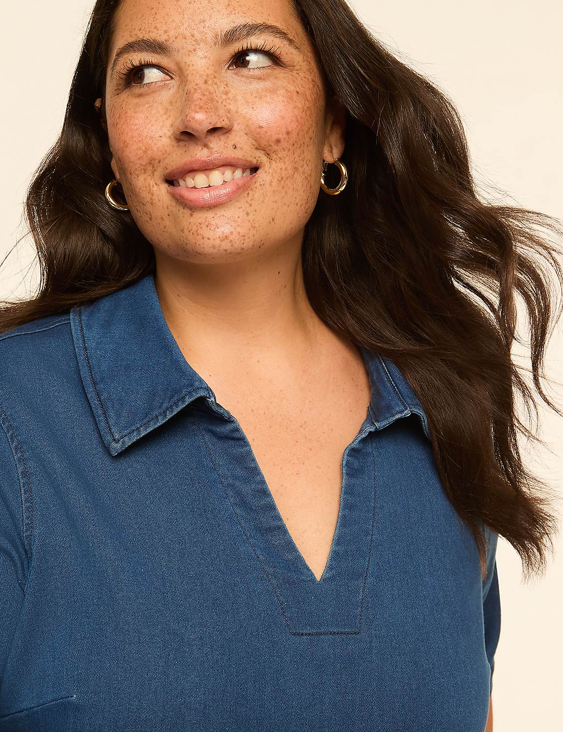 A smiling woman with freckles and dark hair wears a blue denim collared shirt, with a plain, light background. Product Image 3