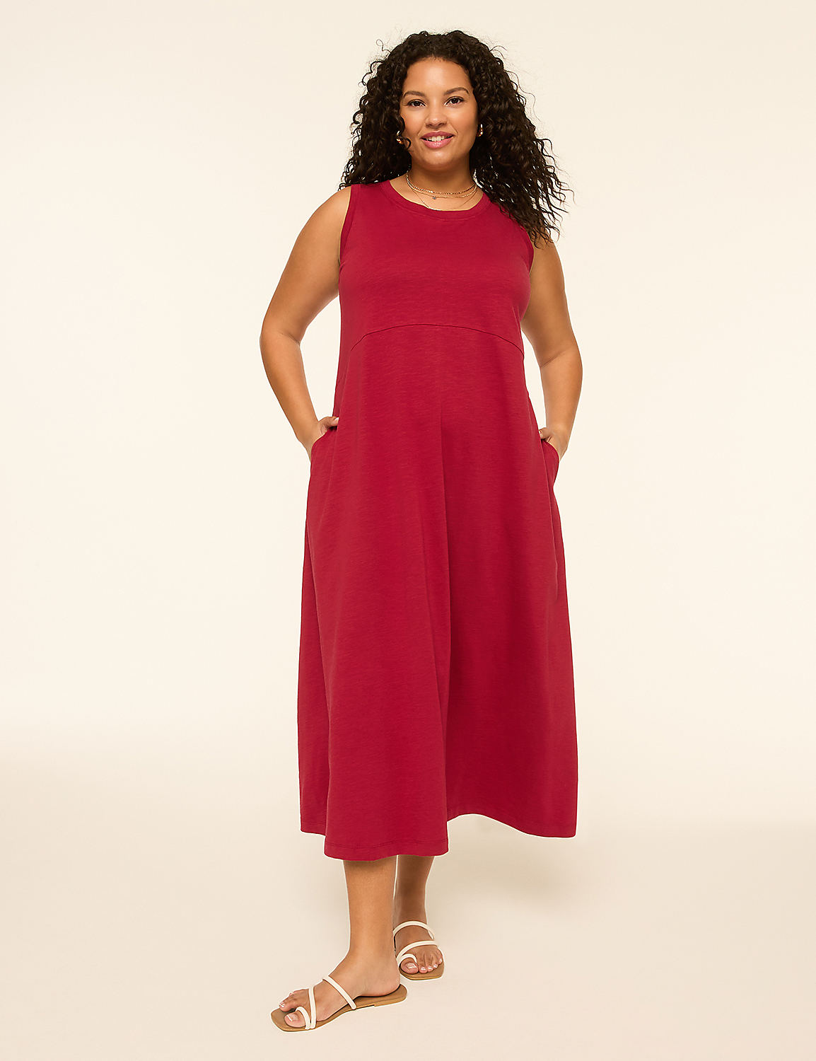 A woman in a red sleeveless dress and white sandals stands with her hands in her pockets against a plain, light background. Product Image 1