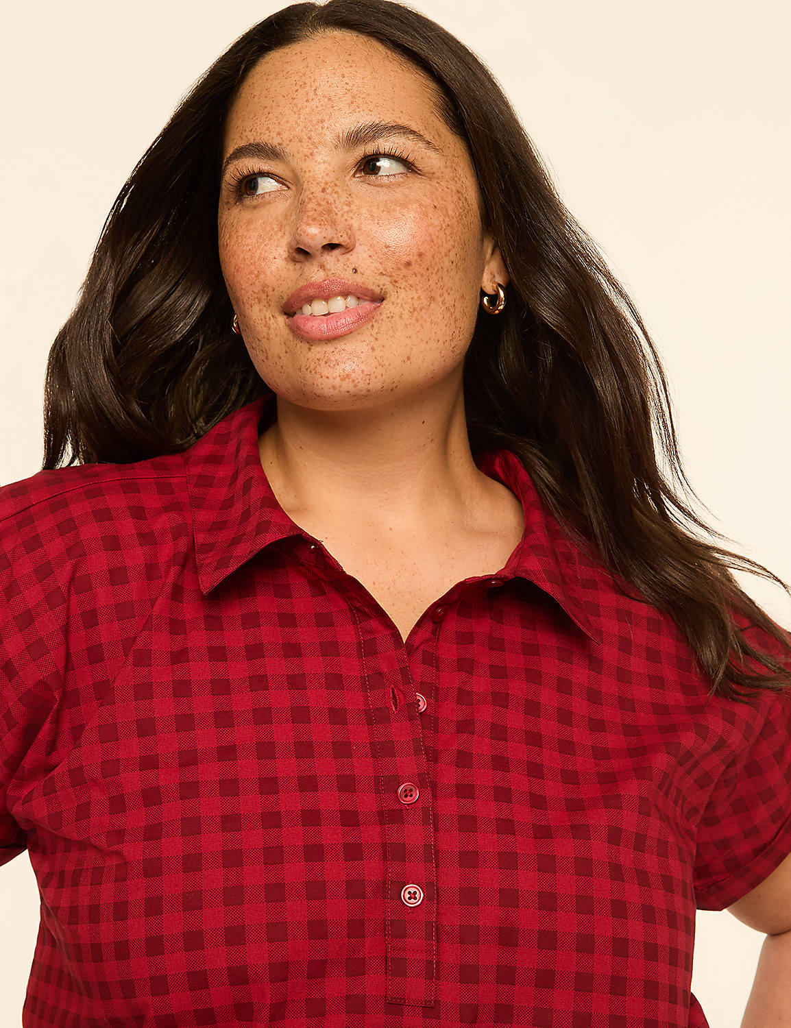A woman with freckles and dark hair smiles slightly in a red gingham shirt against a plain, light background. Product Image 3