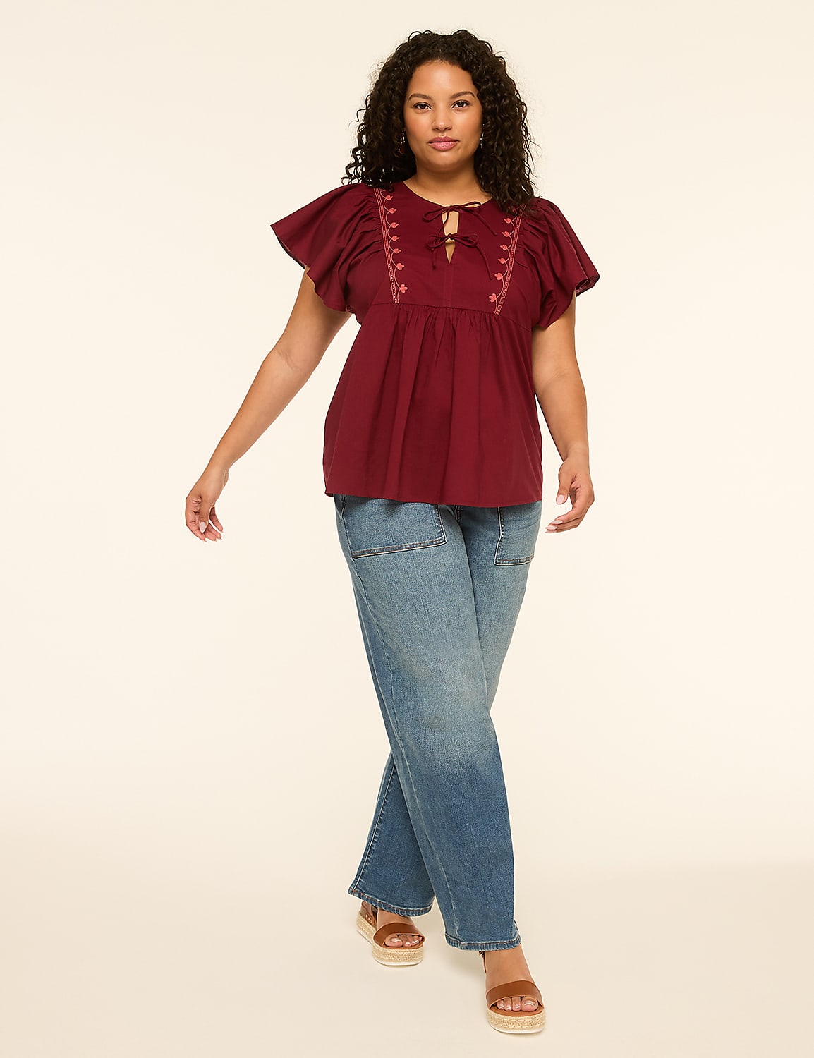 A woman in a burgundy peasant top and blue jeans walks against a plain, light-colored background. Product Image 3