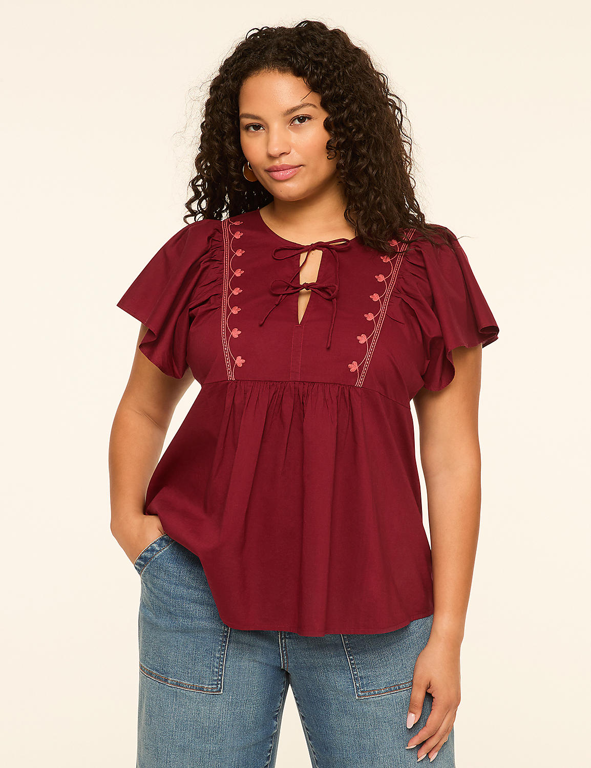A woman in a maroon peasant blouse and blue jeans stands against a plain cream background. Product Image 1