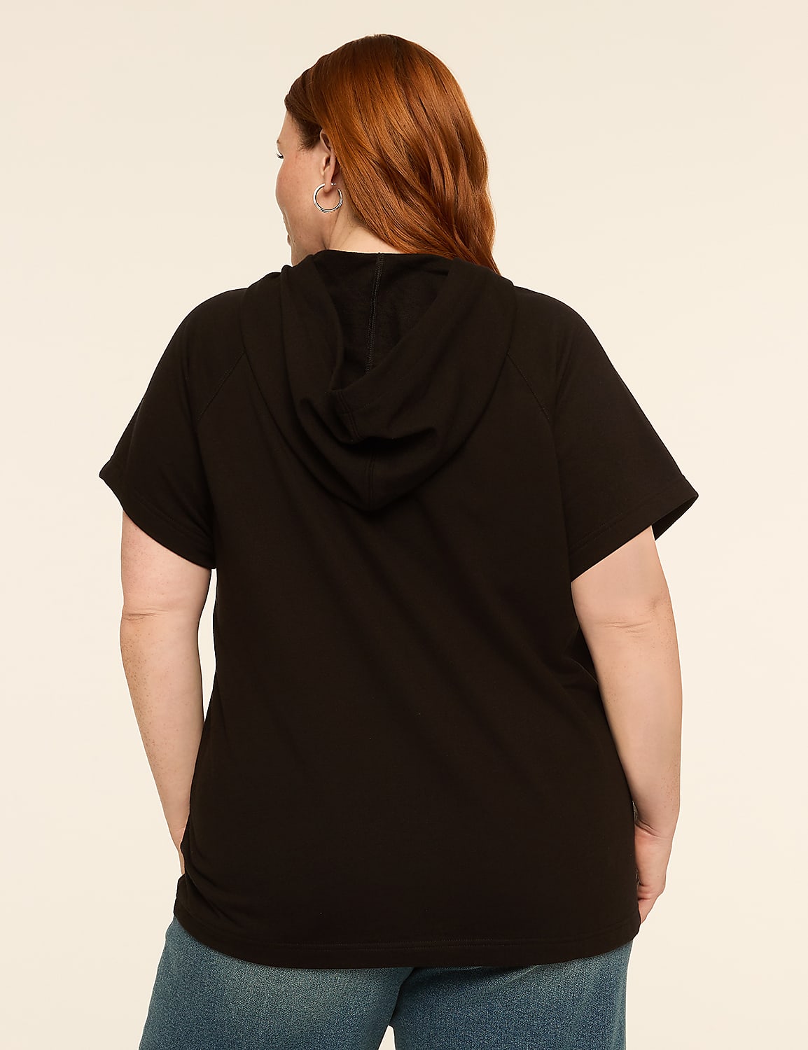 A woman with red hair wearing a black hooded t-shirt and blue jeans stands against a plain, light-colored background. Product Image 2
