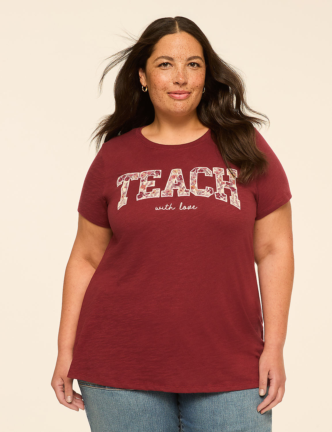 A woman with dark hair and freckles stands in the foreground wearing a maroon t-shirt with "TEACH with love" printed on it, against a plain, light-colored background. Product Image 1
