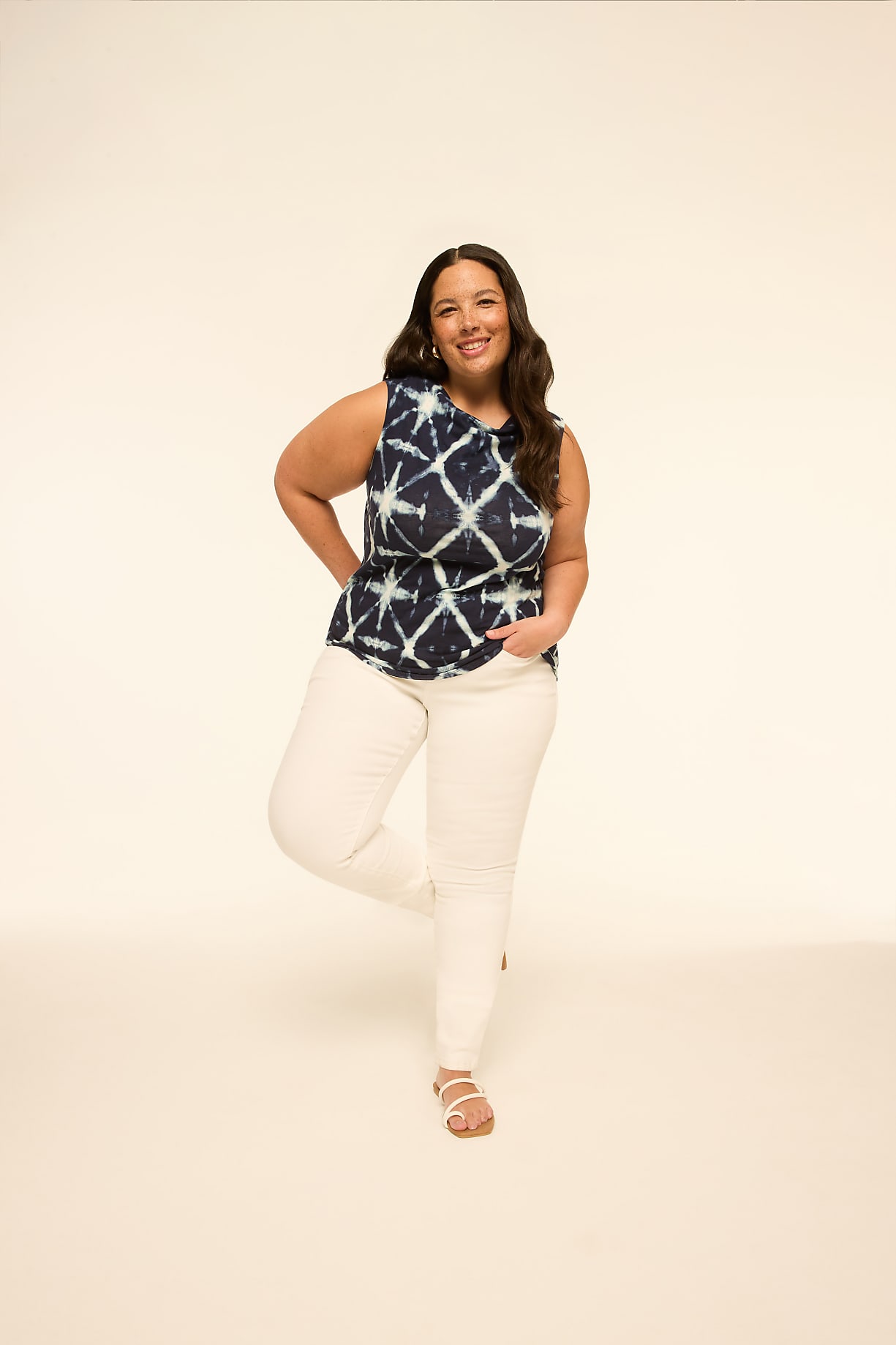A smiling woman in a tie-dye top and white pants stands on one leg against a plain, light-colored background. Product Image 4