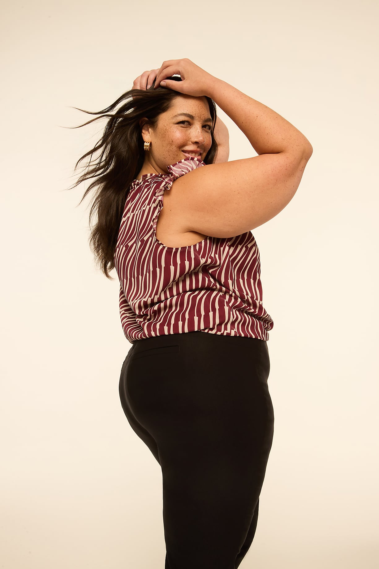 A woman with dark hair and a striped top poses with her hands on her head against a plain, light-colored background. Product Image 6