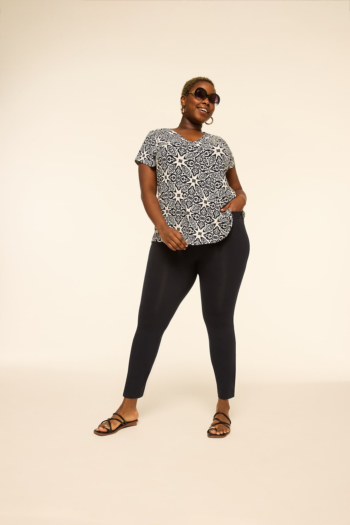 A woman in a patterned shirt and dark pants stands with her hand in her pocket against a plain, light-colored background. Product Image 4